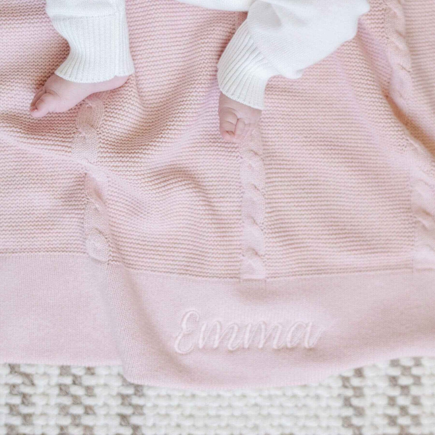Close-up of Saranoni Heirloom Cotton Knit Receiving Blanket with 'Emma' embroidered on it, on a checkered surface.