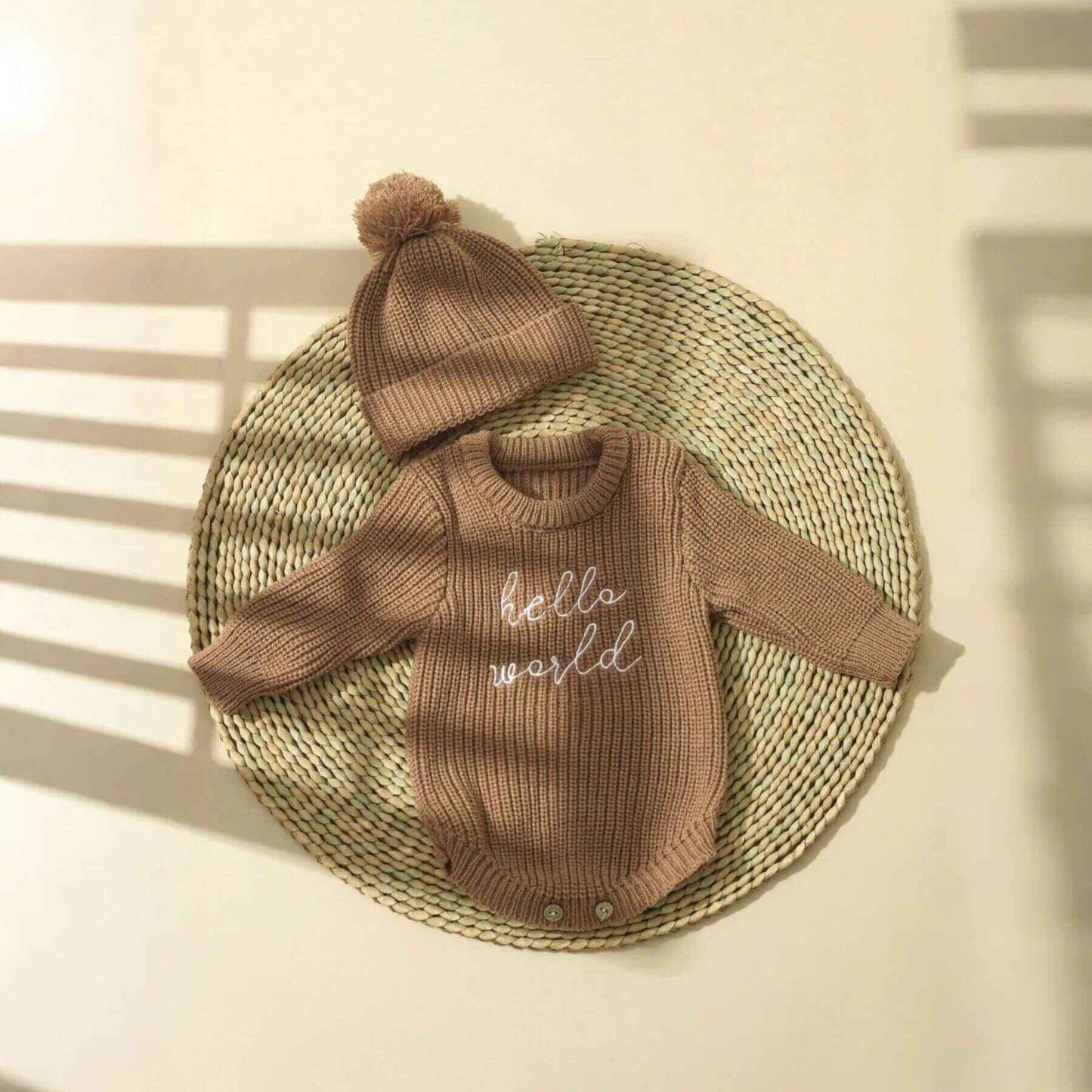Newborn Hello World Knitted Bodysuit Set Brown on a woven mat.