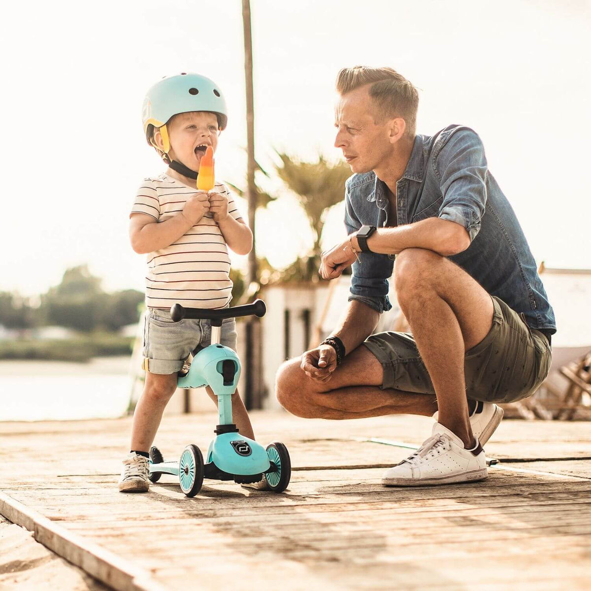 Man and child on a wooden dock with a scooter and helmet