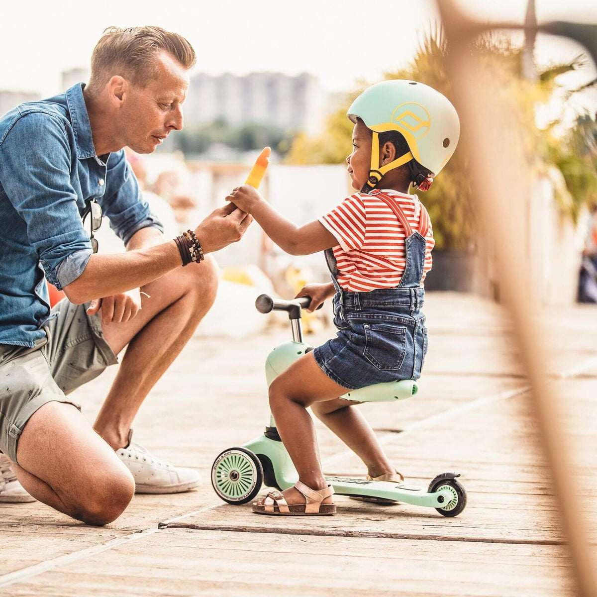 Man teaching a child on a scooter outdoors