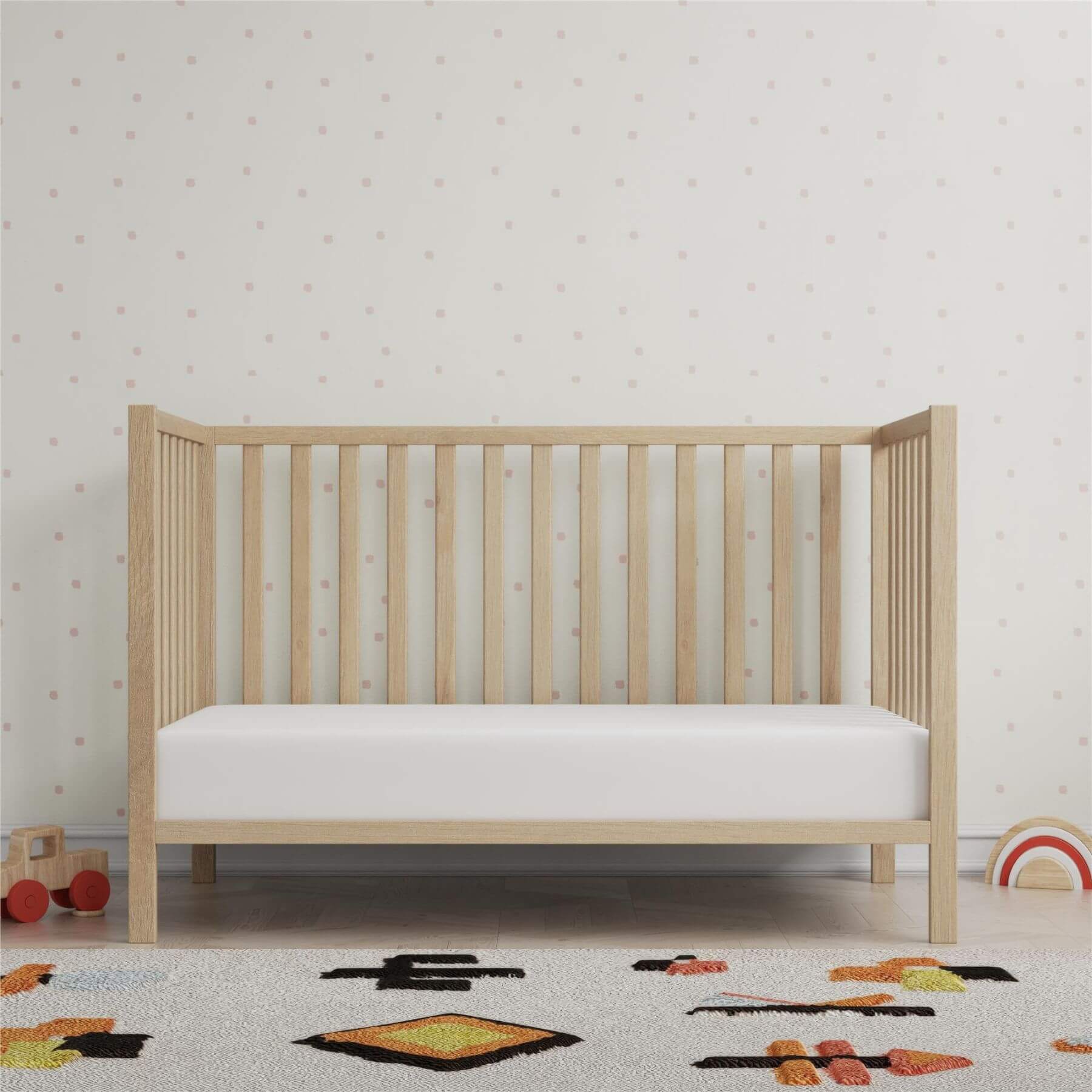 Ivey 3-in-1 Convertible Crib Light Natural with white mattress in a room with toys and patterned wallpaper