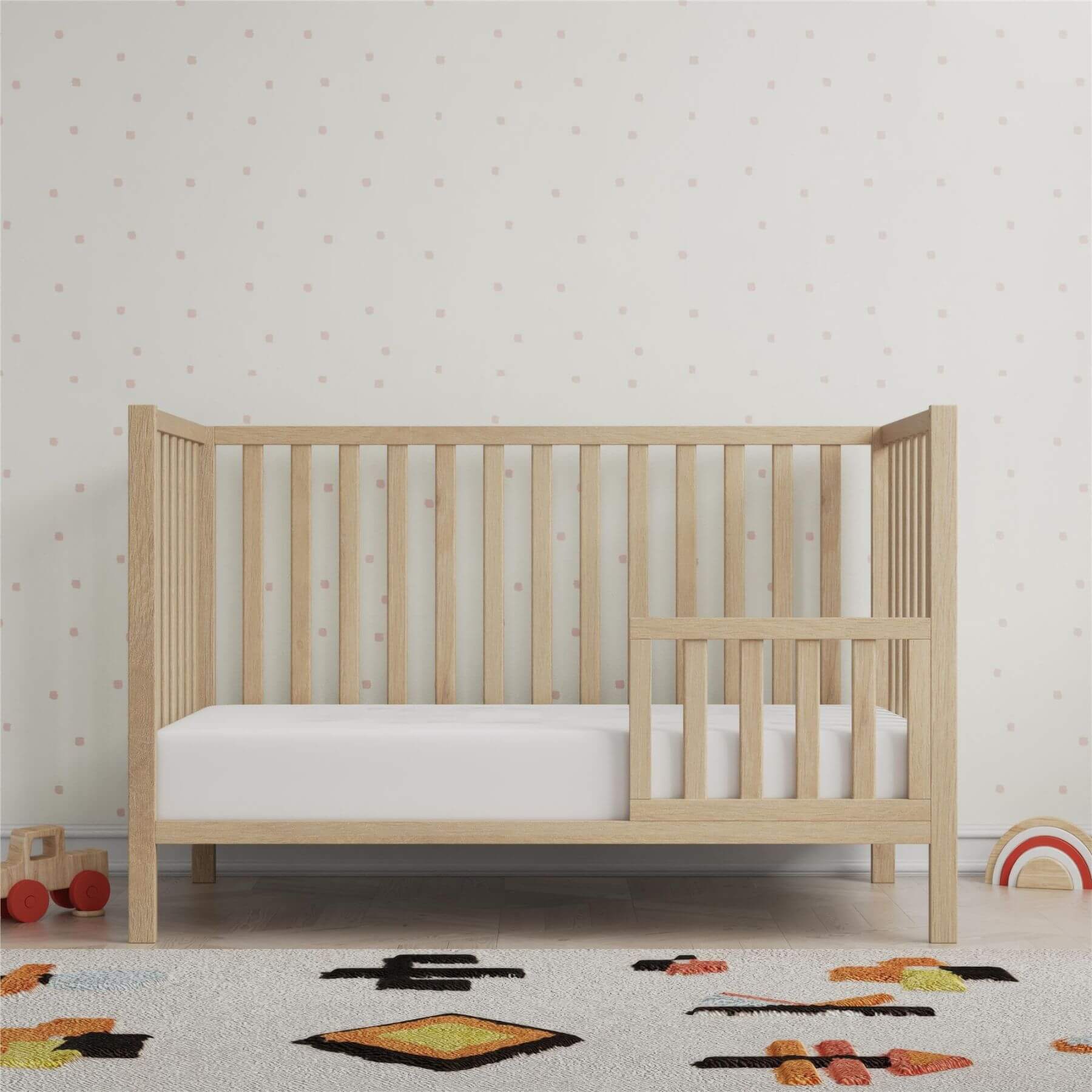 Ivey 3-in-1 Convertible Crib Light Natural with white mattress in a room with toys and a patterned rug.
