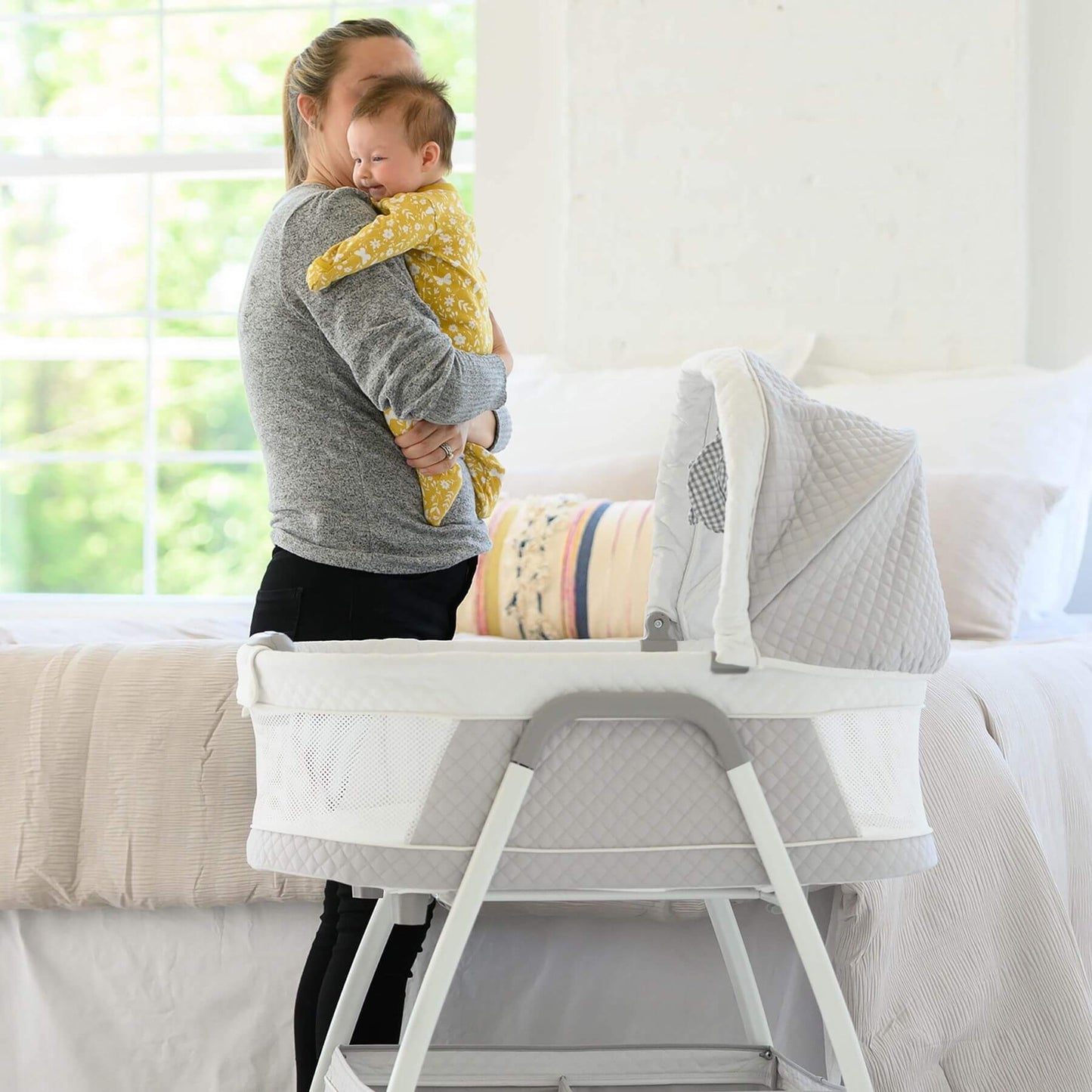 Mom Holding Baby next to TruBliss Journey 3-in-1 Bassinet