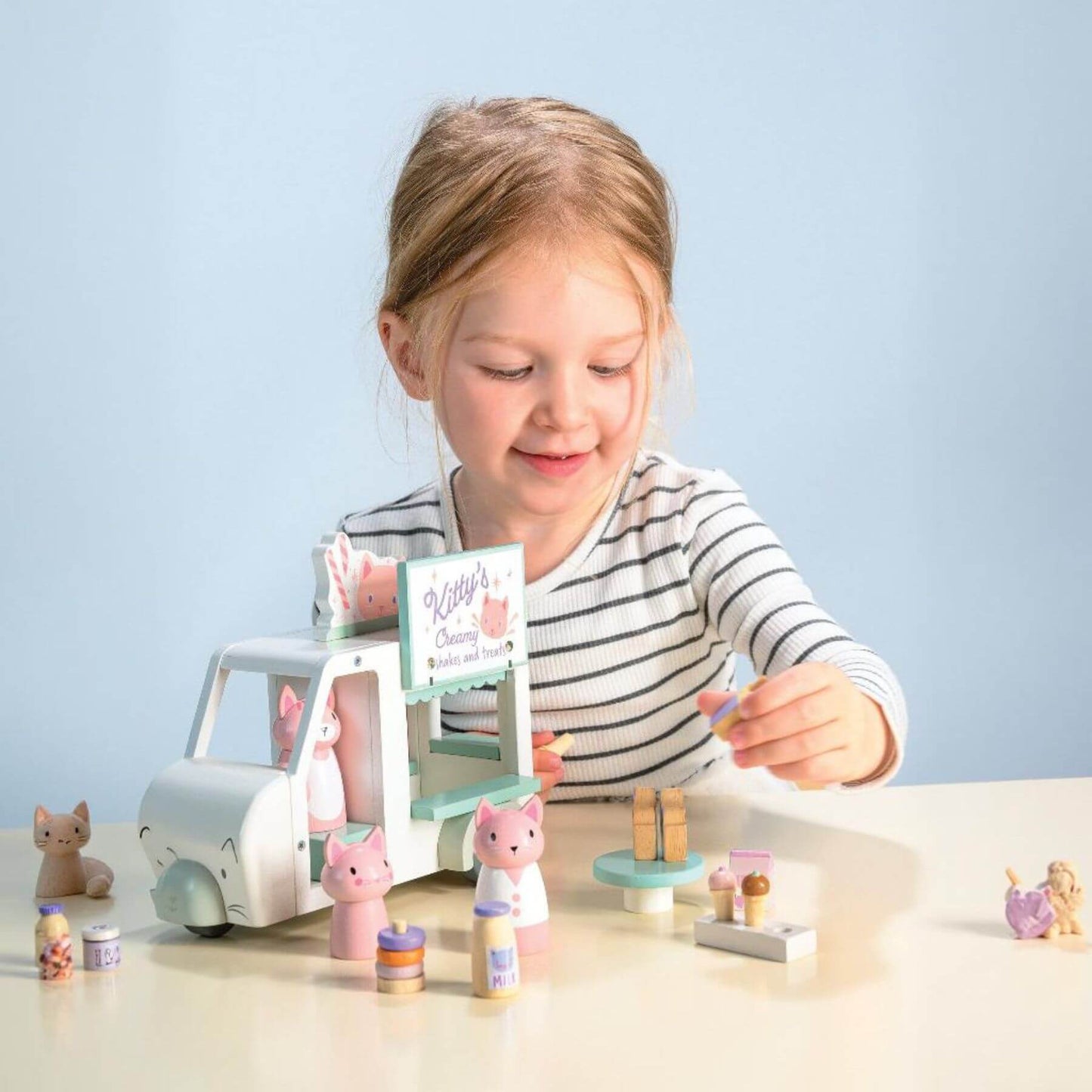 Child playing with Tender Leaf Kitty's Milkshake Van on a table against a light blue background
