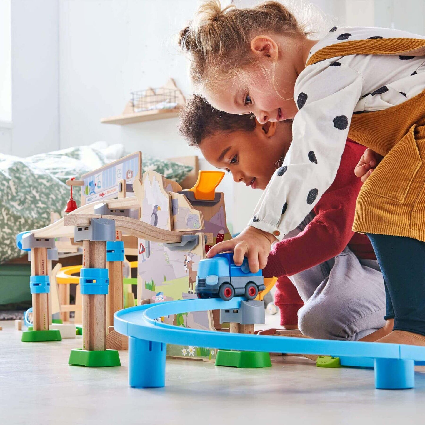 Two children playing with HABA USA Kullerbu Mountain Adventure Track Set on a light-colored floor.