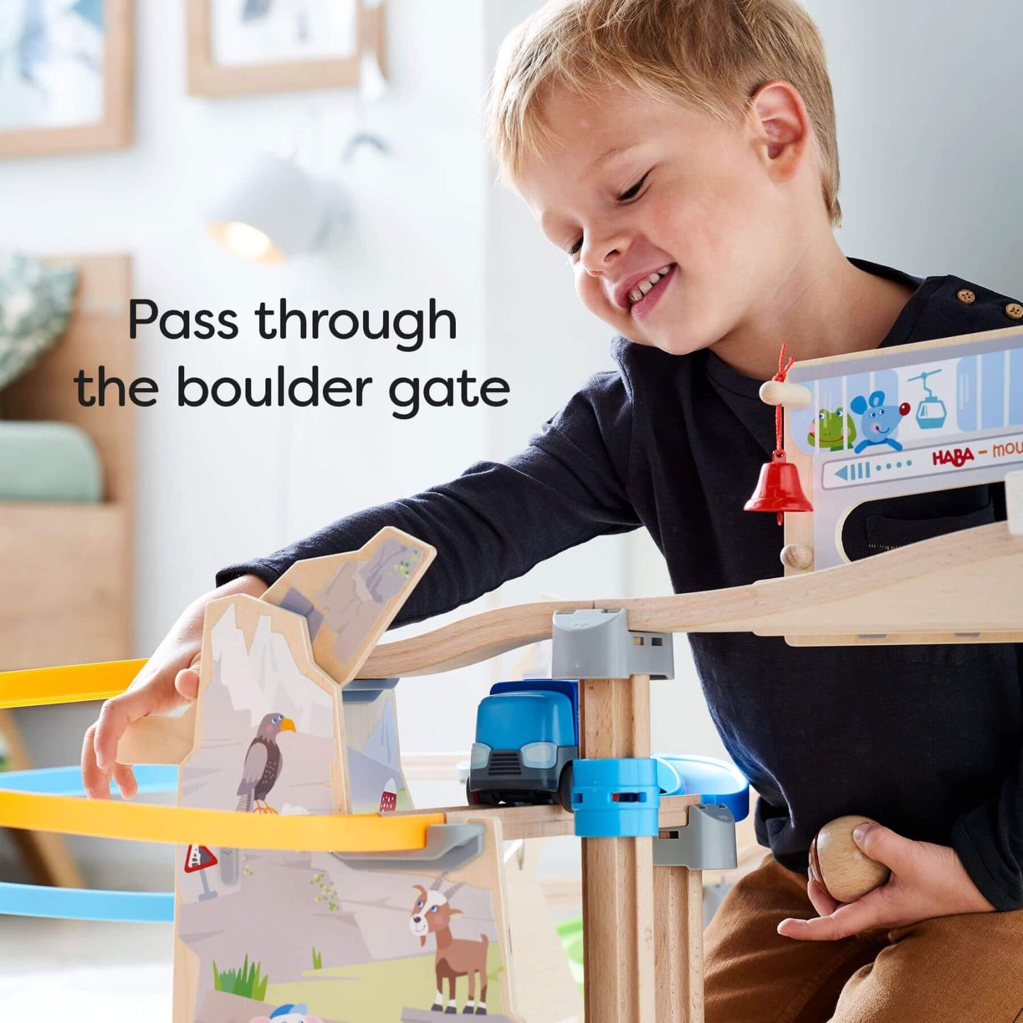Child playing with HABA USA Kullerbu Mountain Adventure Track Set, holding a boulder, with text 'Pass through the boulder gate'.