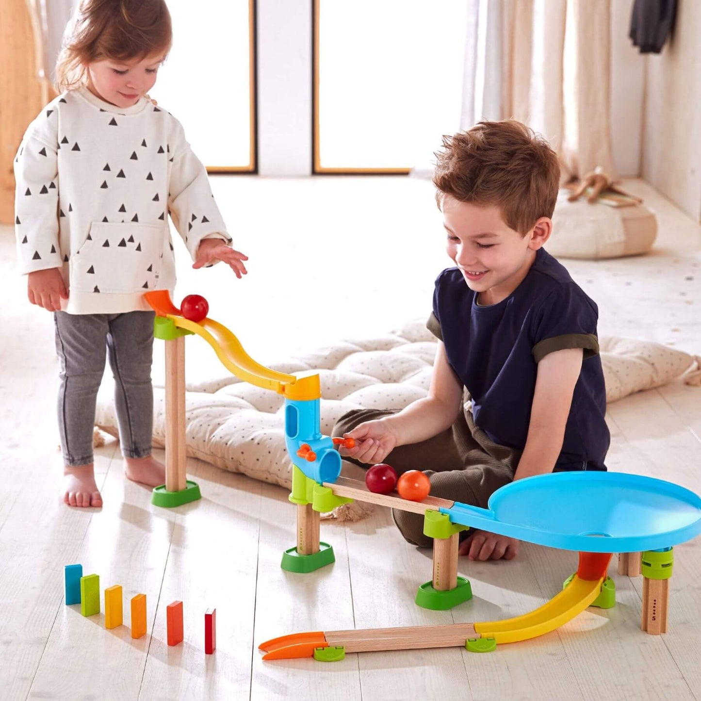 Two children playing with HABA USA Kullerbu Traffic Jam Ball Track Set on a light wooden floor.