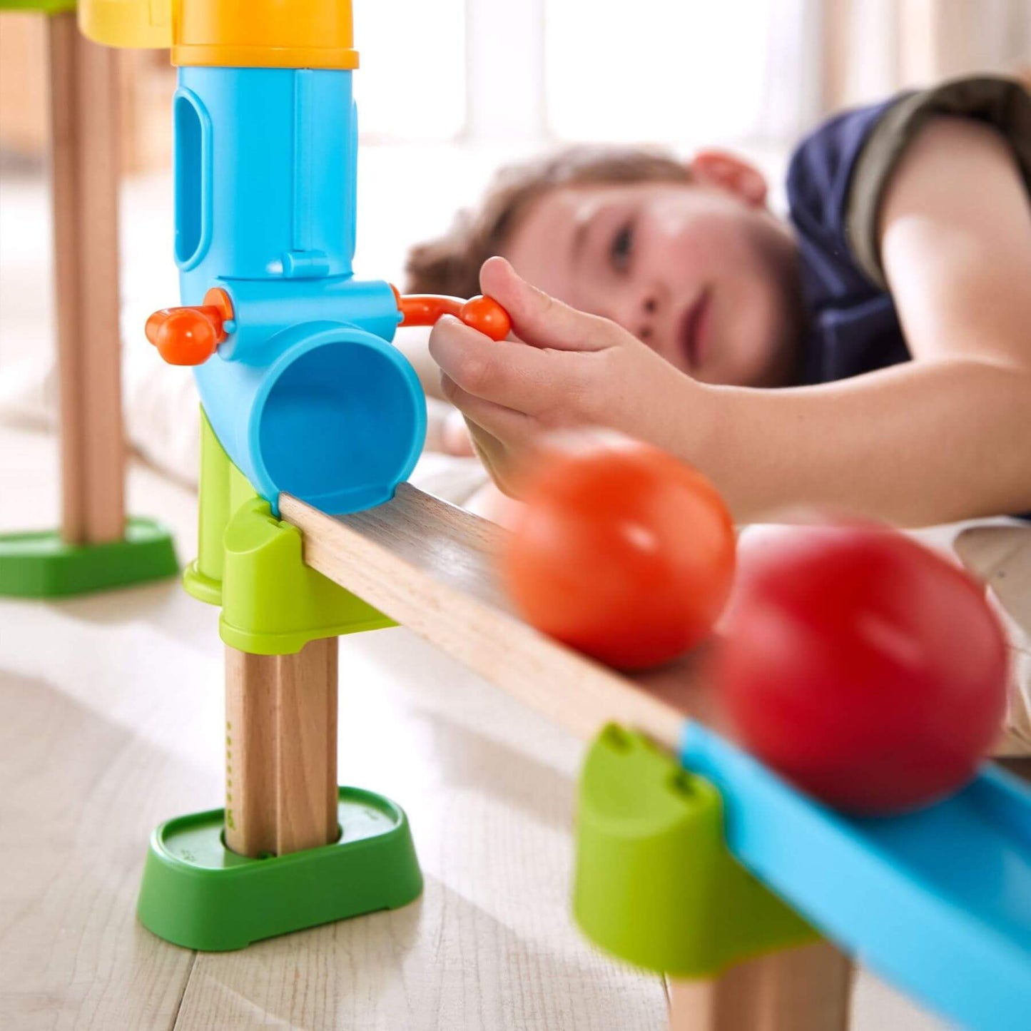 Child playing with Kullerbu Traffic Jam Ball Track Set on a wooden floor.