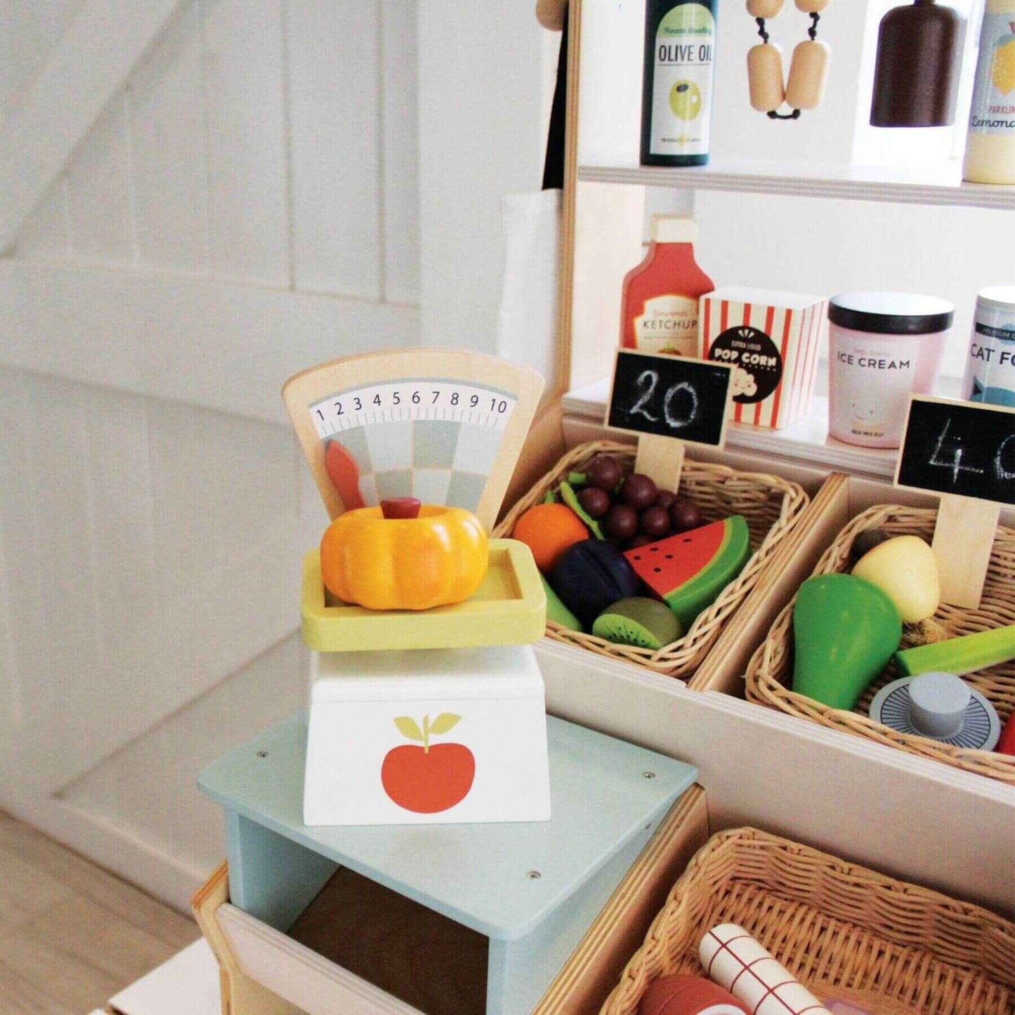 Toy kitchen set with toy fruits, vegetables, and a scale on a wooden surface.