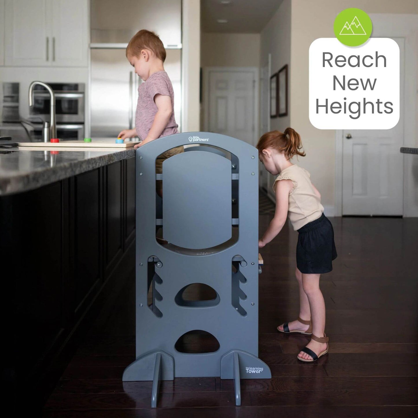 Boy Standing on Little Partners Limited Edition Learning Tower Grey, with a Girl Drawing on the Blackboard