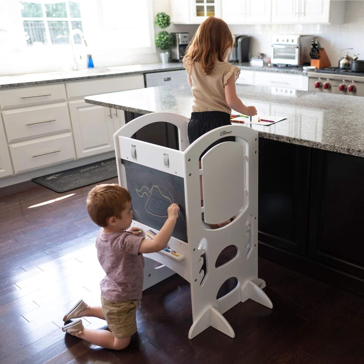 Girl Standing on Little Partners Limited Edition Learning Tower White, with a Boy Drawing on the Blackboard
