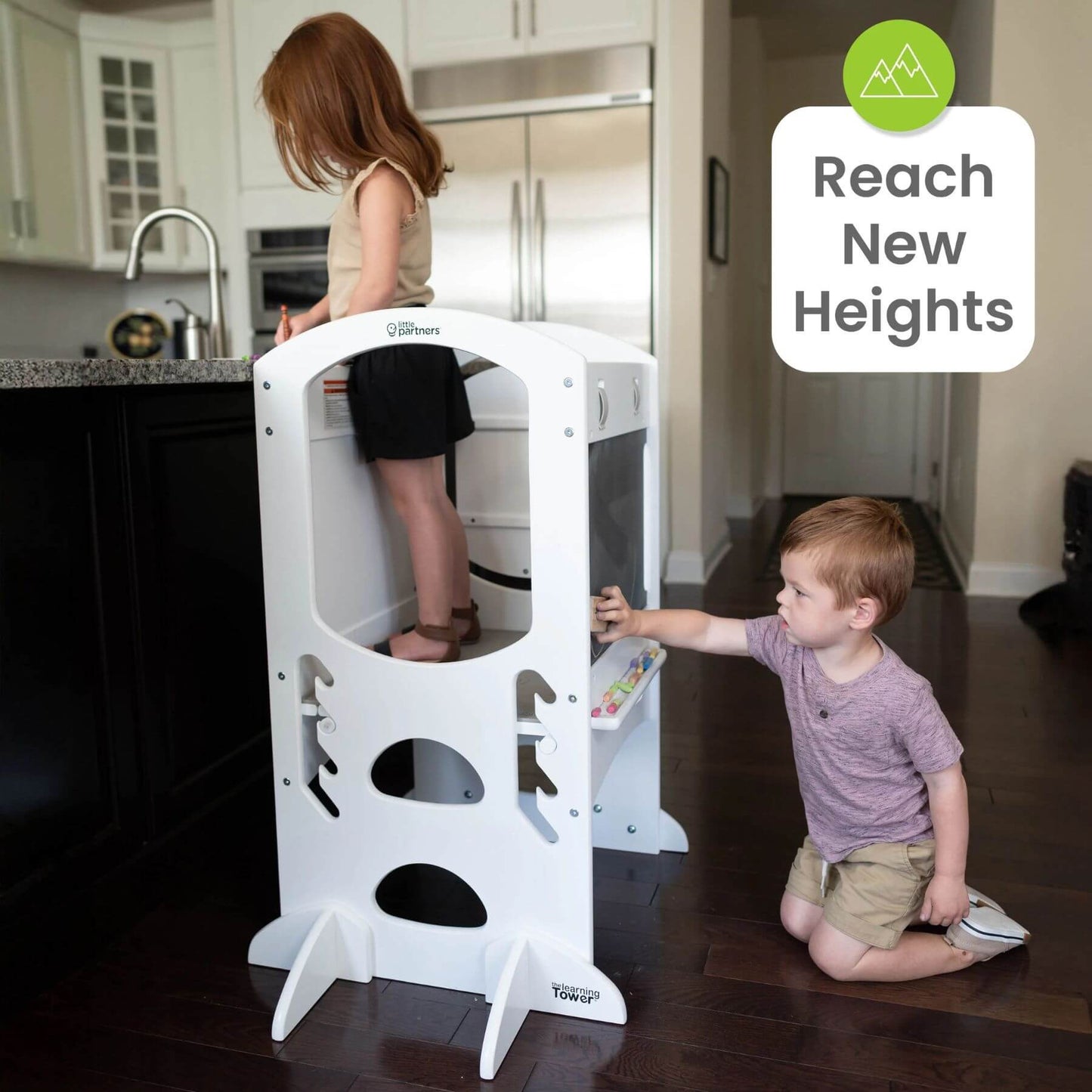 Girl Standing on Little Partners Limited Edition Learning Tower White, with a Boy Drawing on the Blackboard