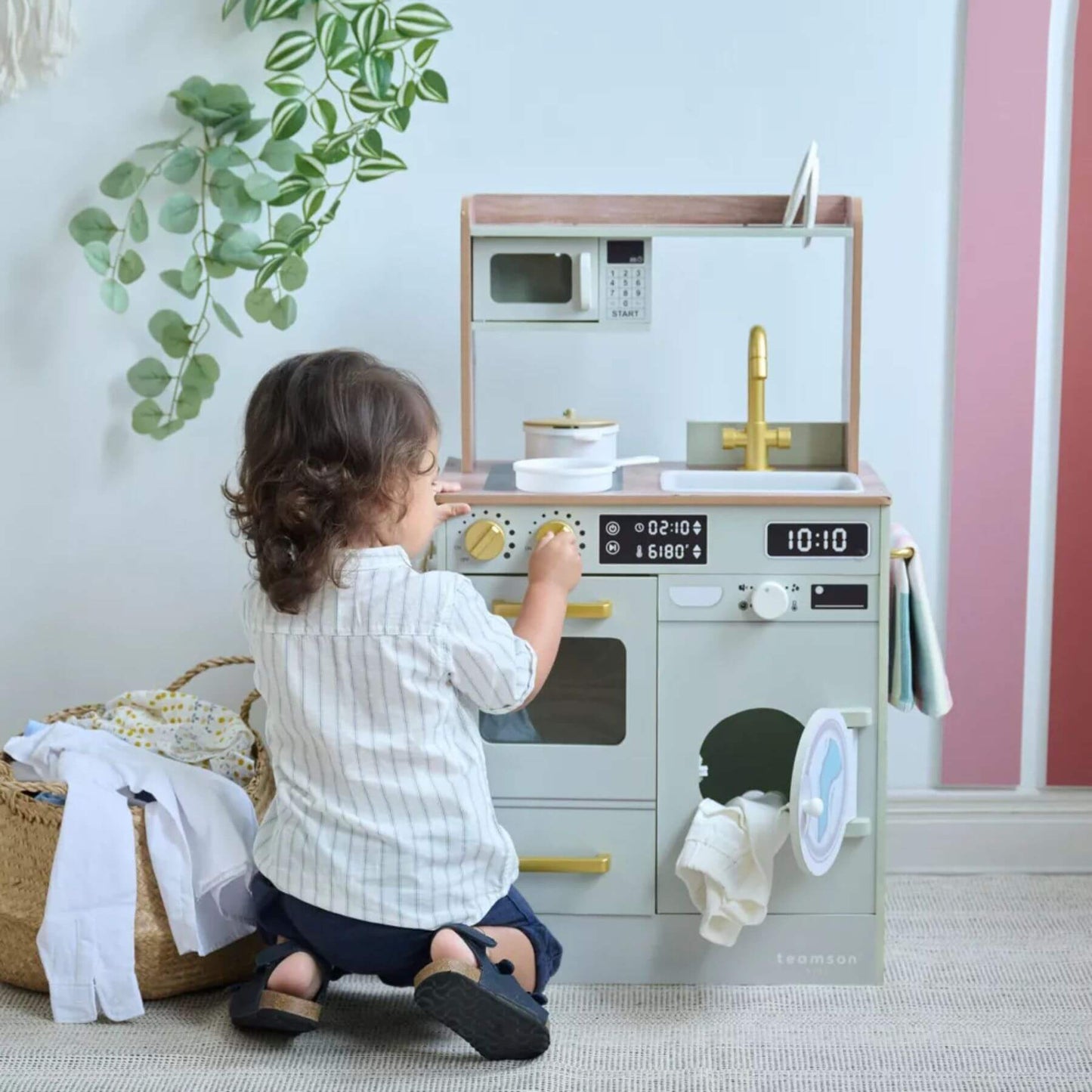 Child playing with Teamson Kids Little Chef Lake Tahoe Wooden Play Kitchen Green in a room with a plant and basket.