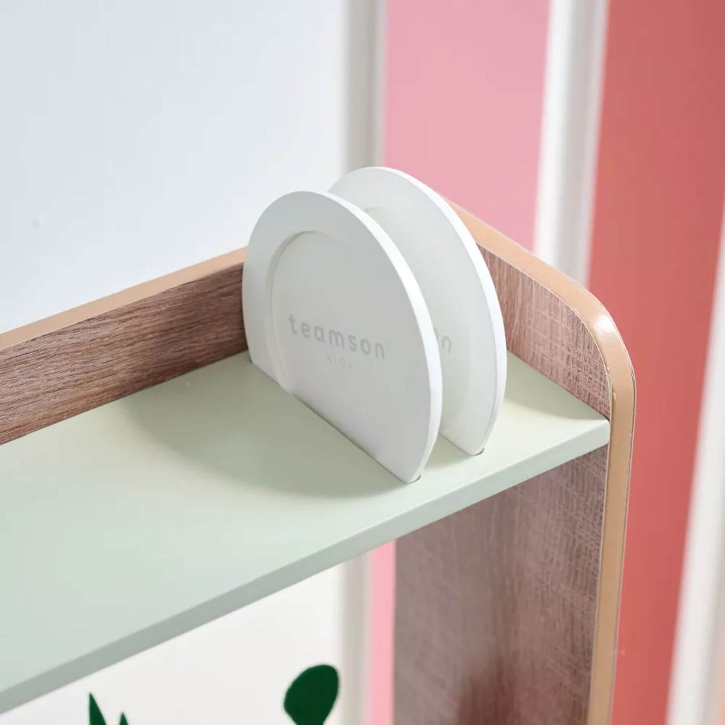 White container with 'teamson' branding on a wooden shelf against a pink wall.
