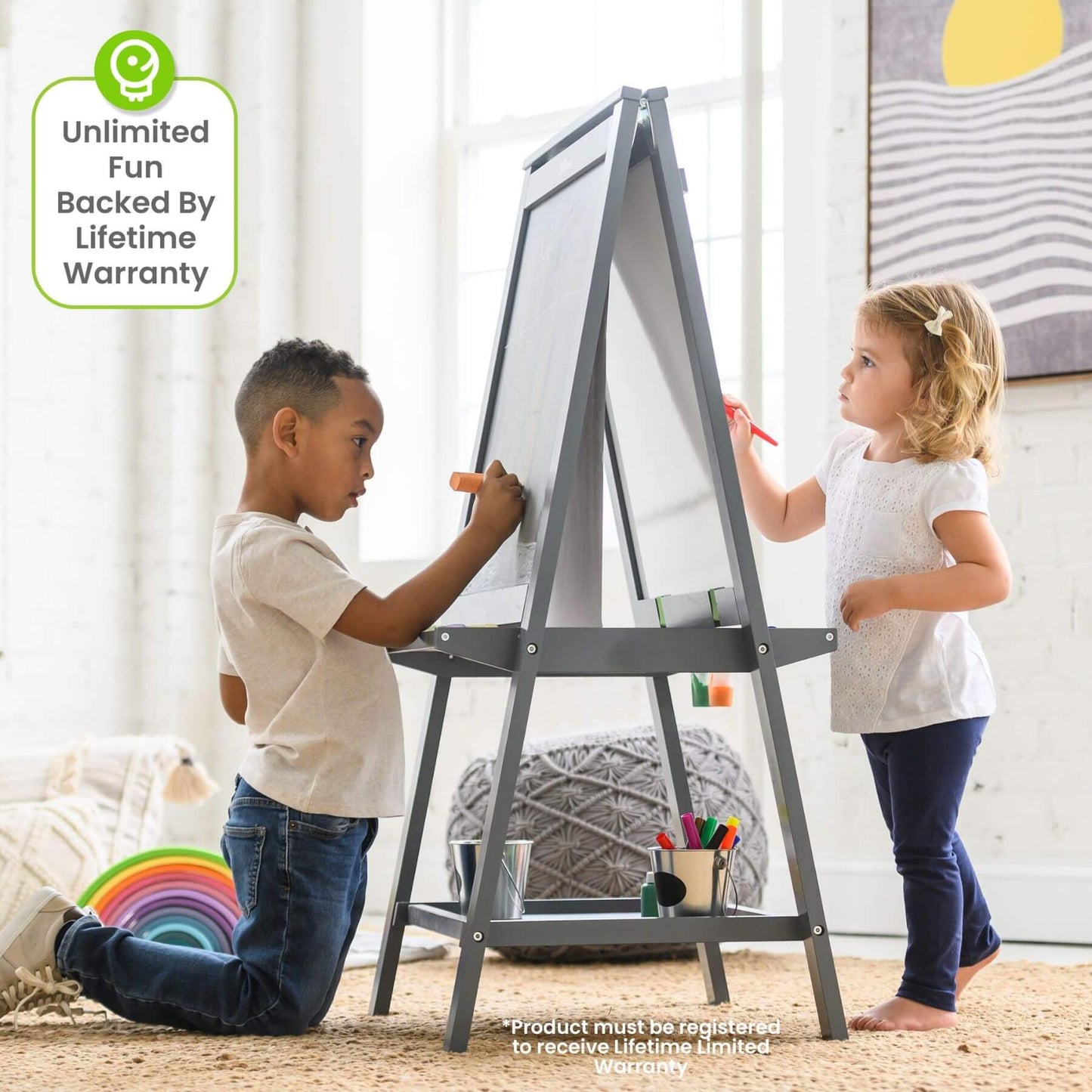 Two children drawing on a Little Partners Folding Artist EZ Easel Grey in a room with a rainbow decoration.