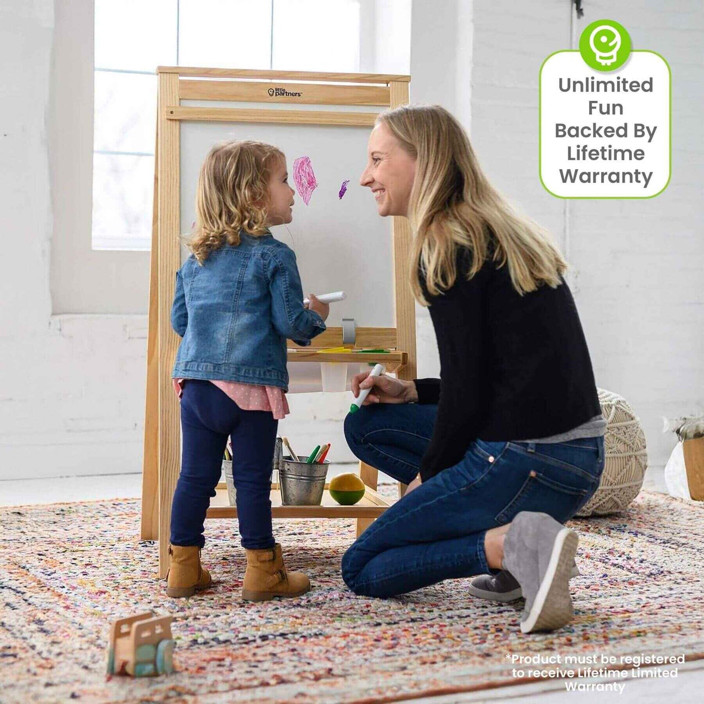 Woman and child playing with a Little Partners Folding Artist EZ Easel Natural in a room with a colorful rug.