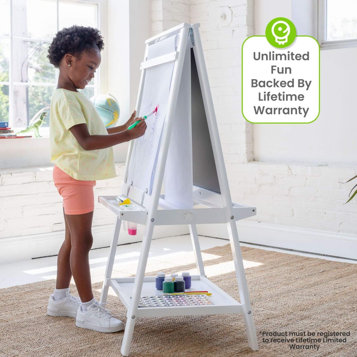 Child drawing on a Little Partners Folding Artist EZ Easel White with art supplies in a bright room.