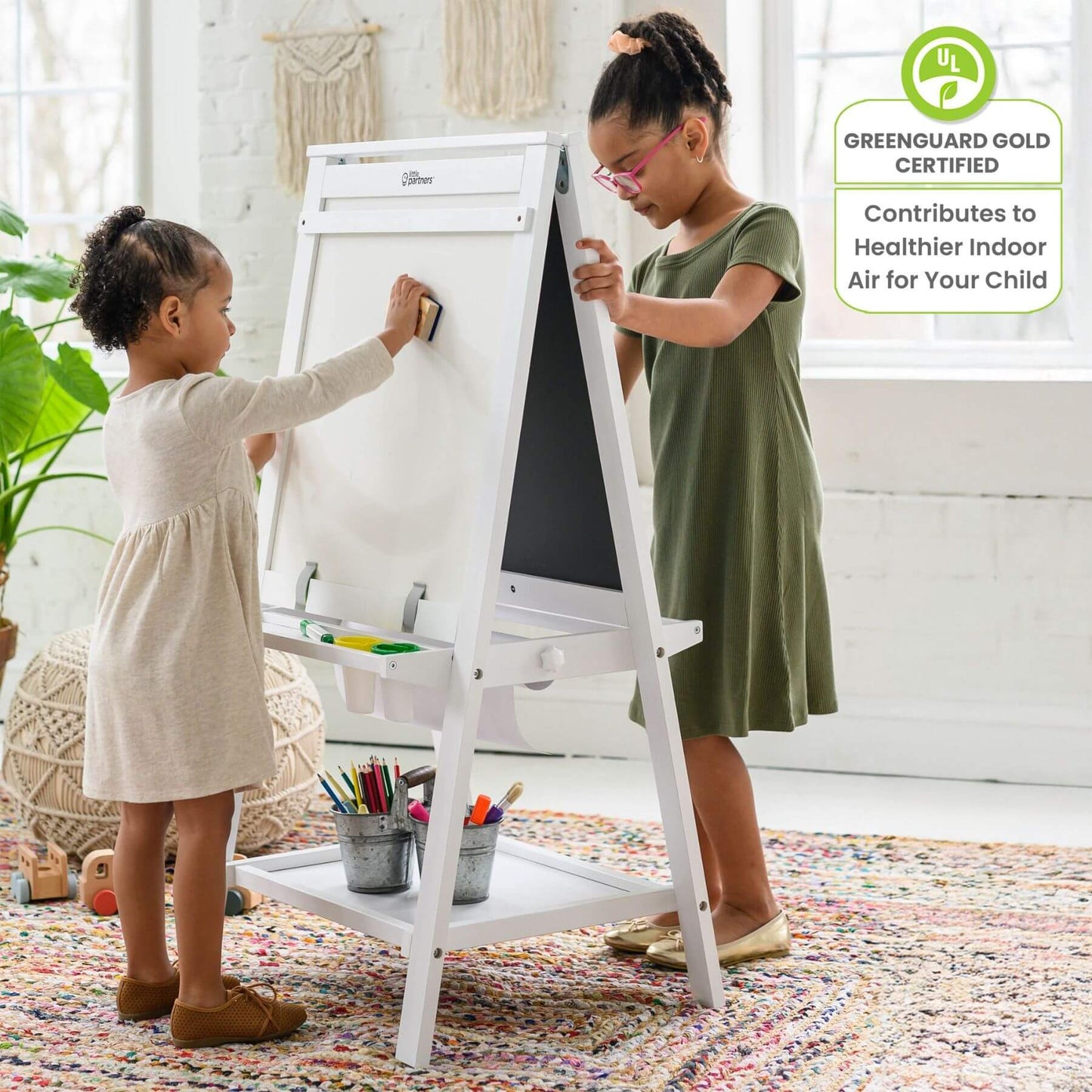Two children using a Little Partners Folding Artist EZ Easel White in a bright room with a green certification badge on the right.