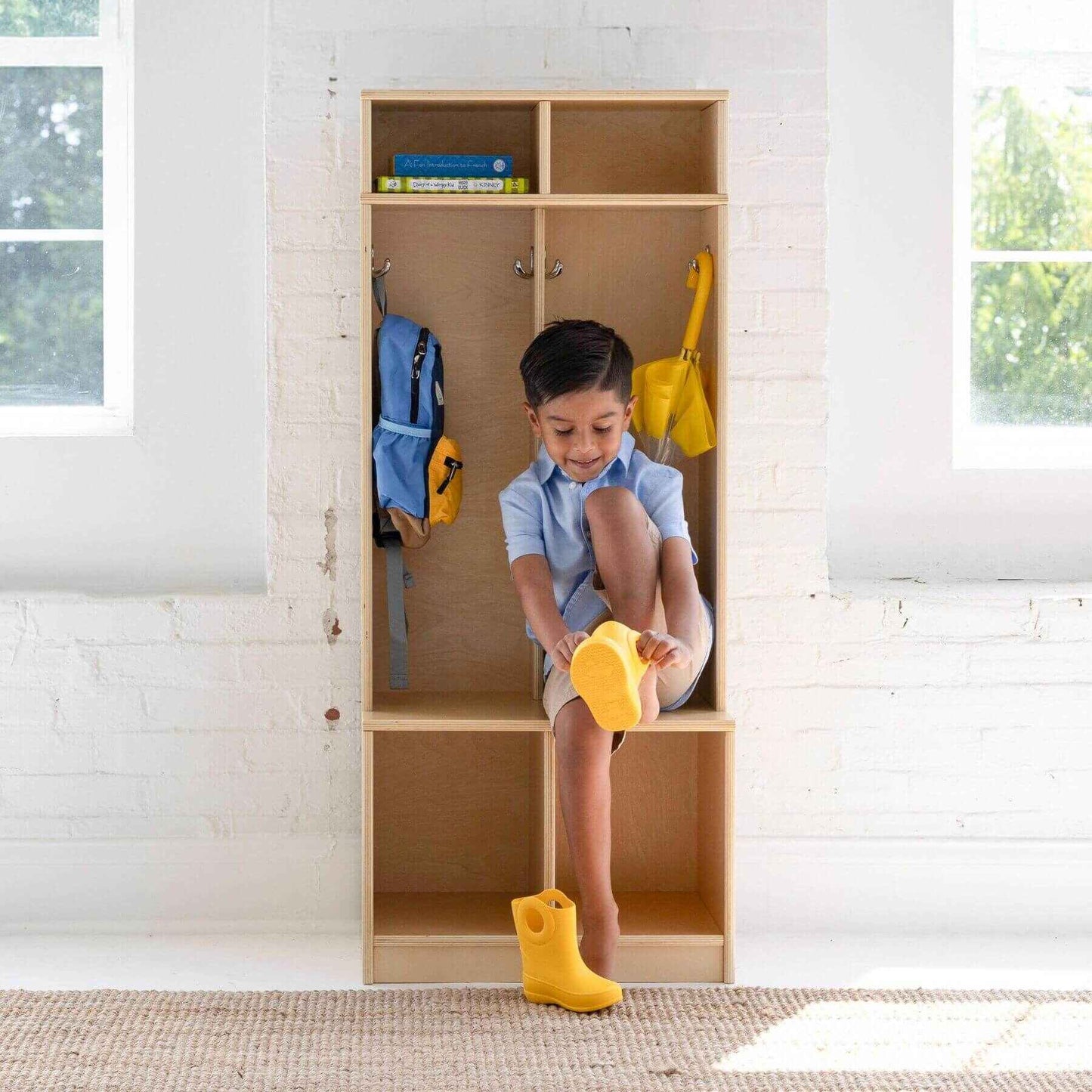 Child sitting inside Little Partners Learn 'N Store Cubby Natural, wearing yellow boots and holding a yellow toy.