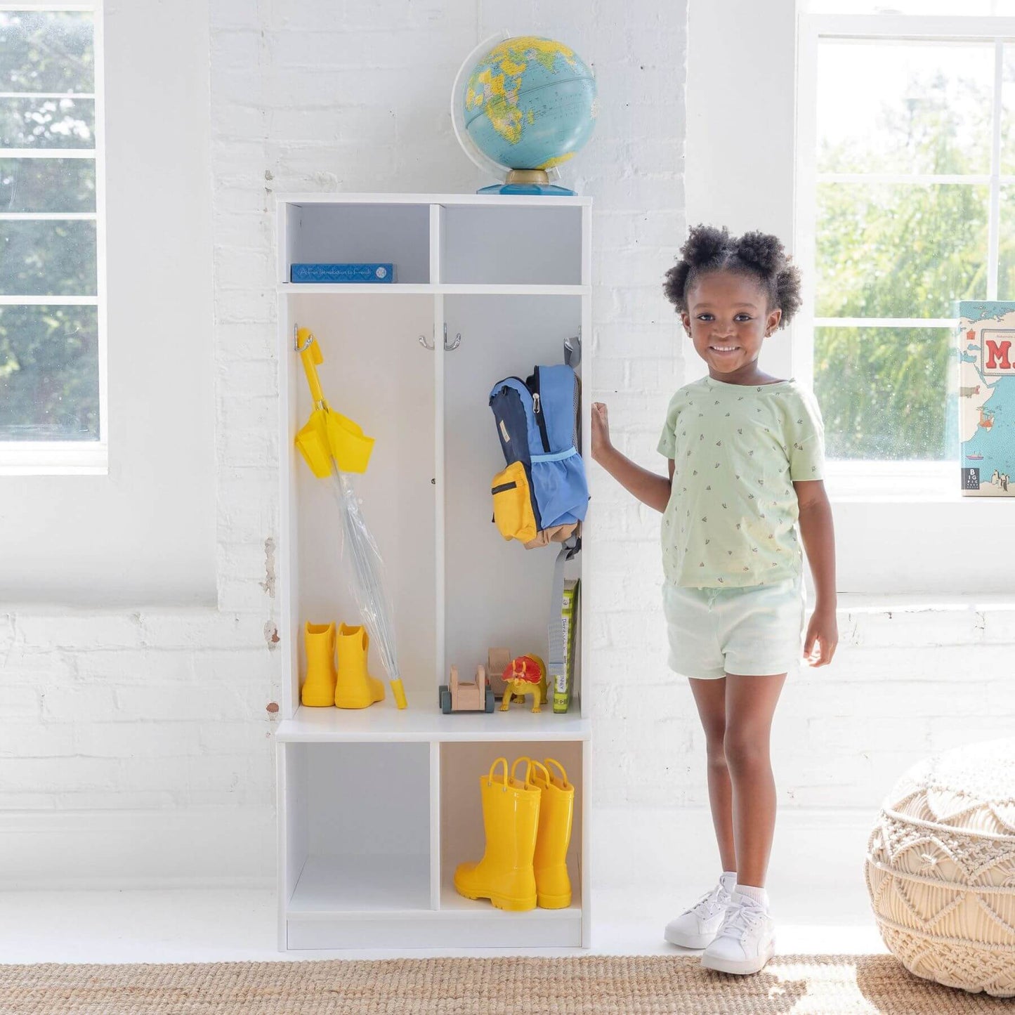Child standing next to Little Partners Learn 'N Store Cubby with various items including yellow boots and a blue bag.