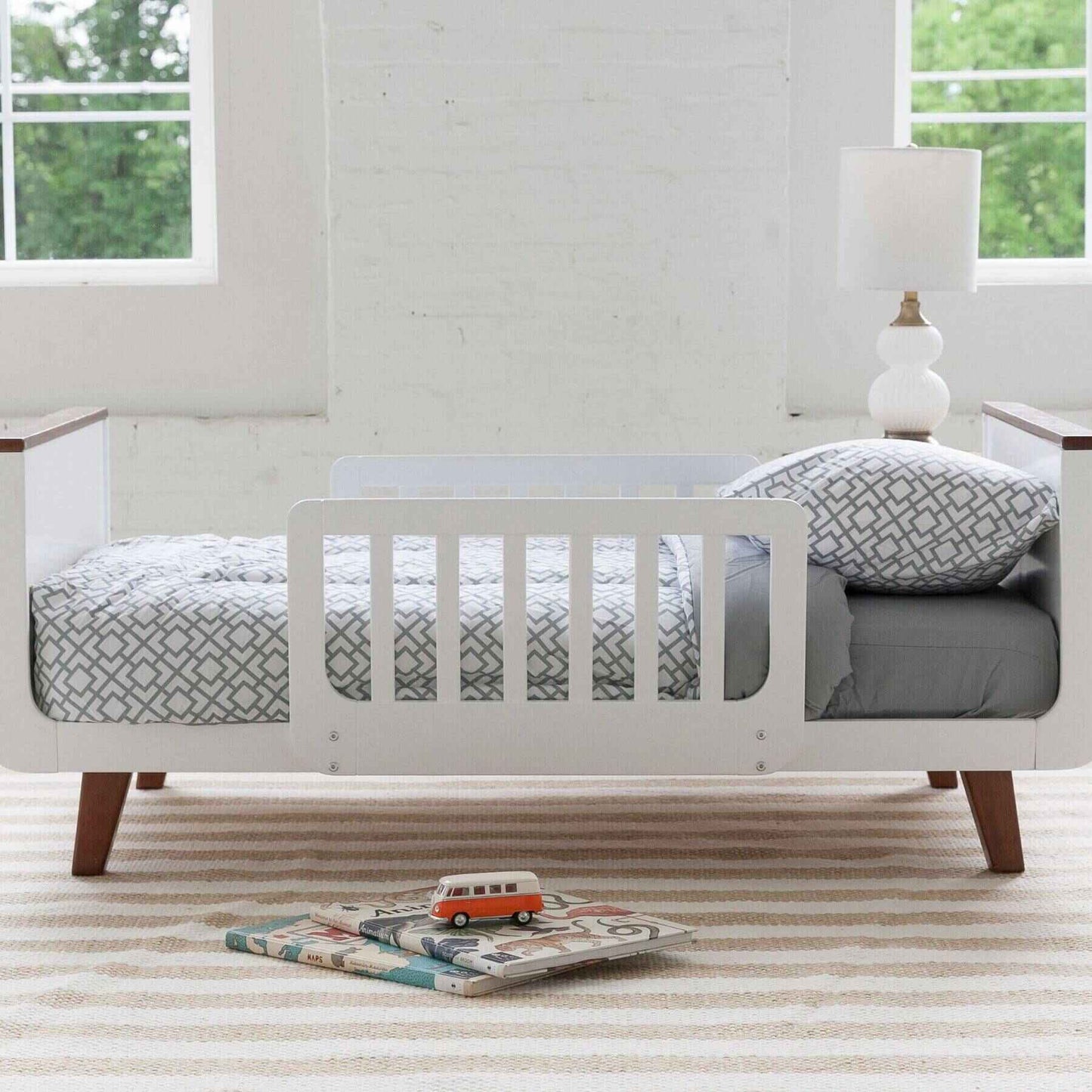 Little Partners MOD Toddler Bed Espresso & White in a room with large windows and a lamp.