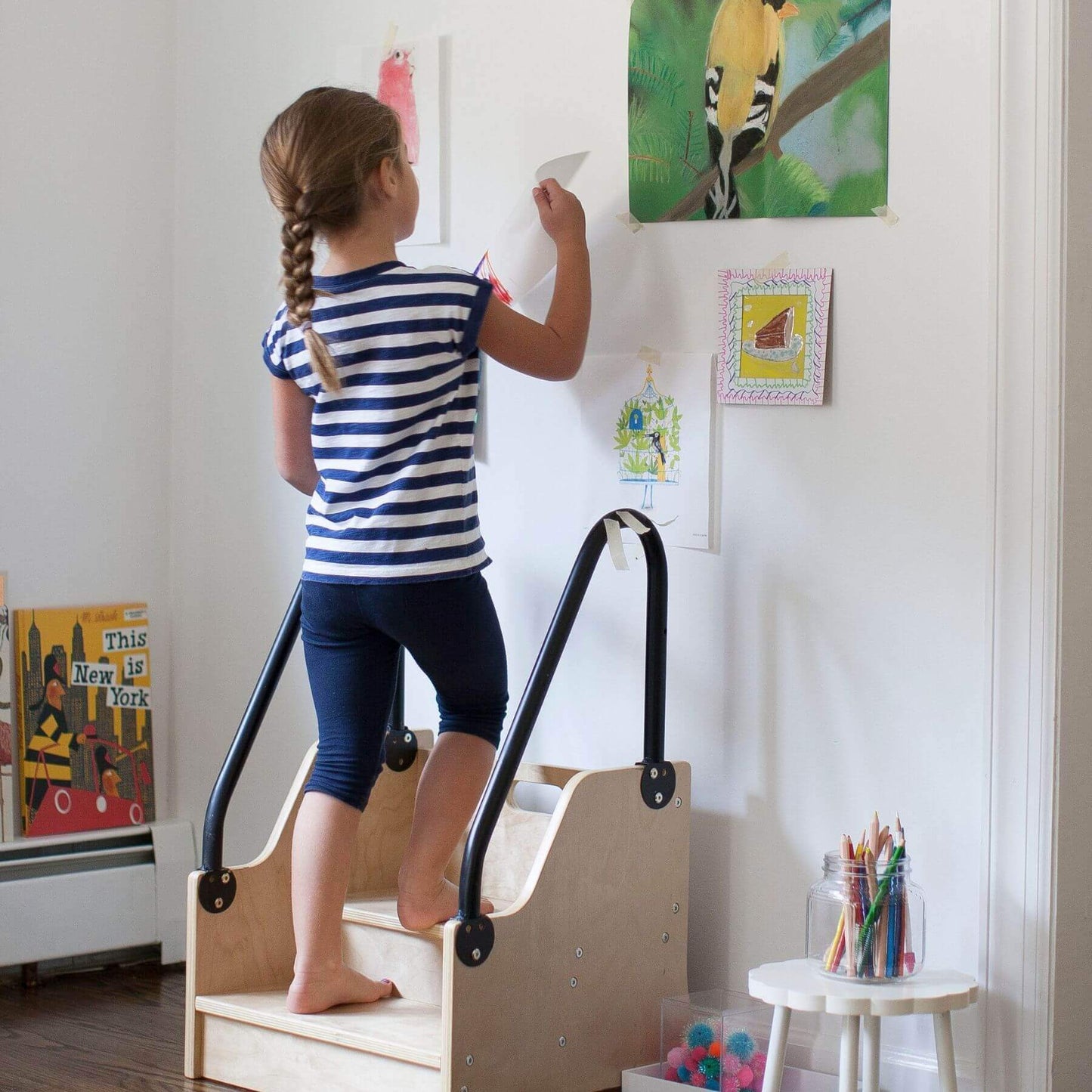 Child using a Little Partners ReachUp Step Stool to reach artwork on a wall