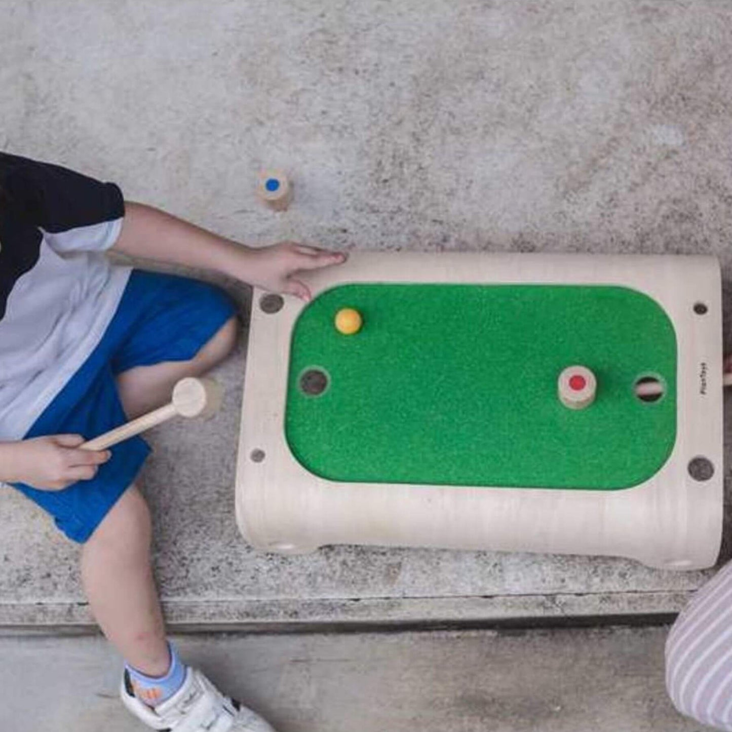 Child playing with PlanToys Magnetic Board Game on a concrete floor