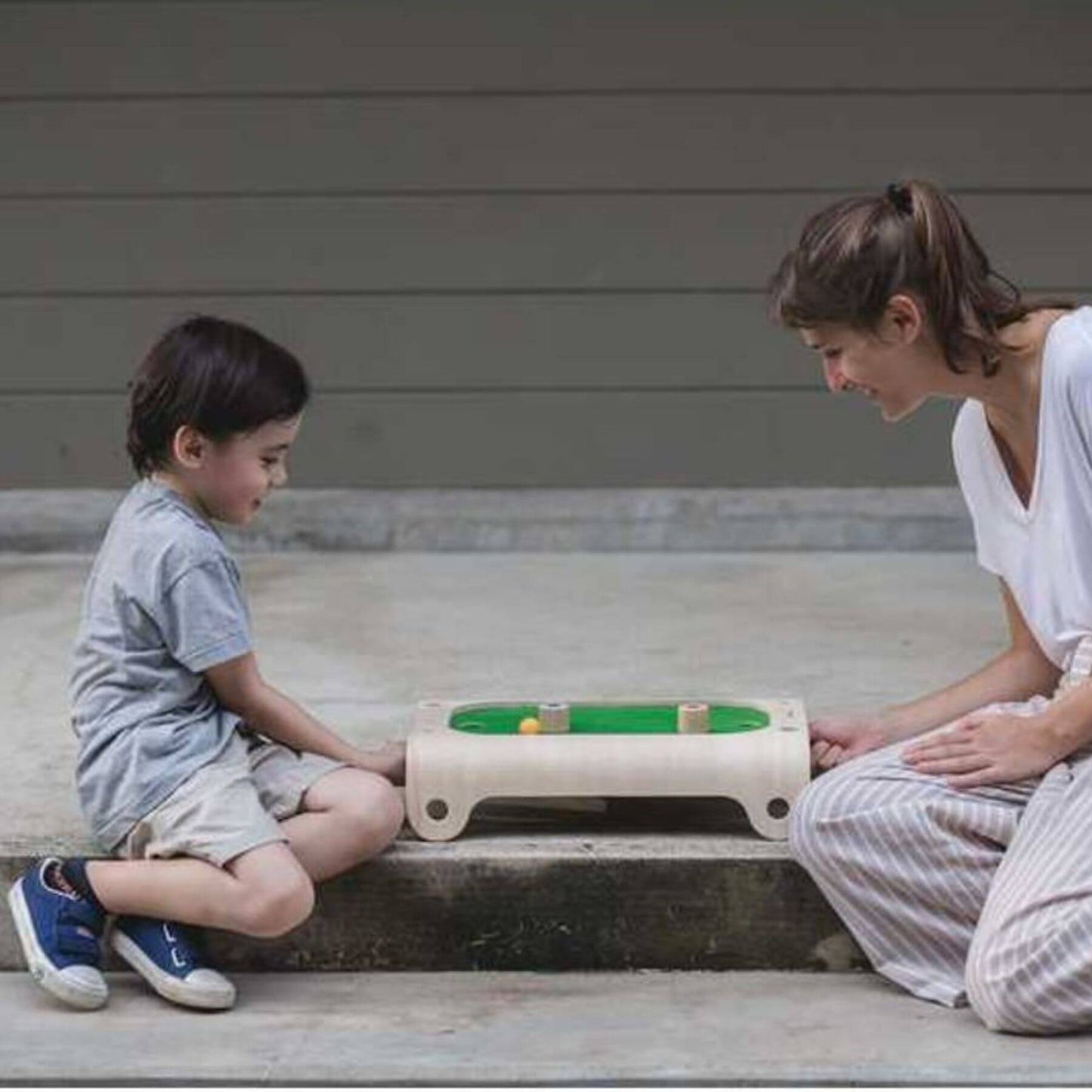 Woman and child playing with PlanToys Magnetic Board Game on a wooden floor.