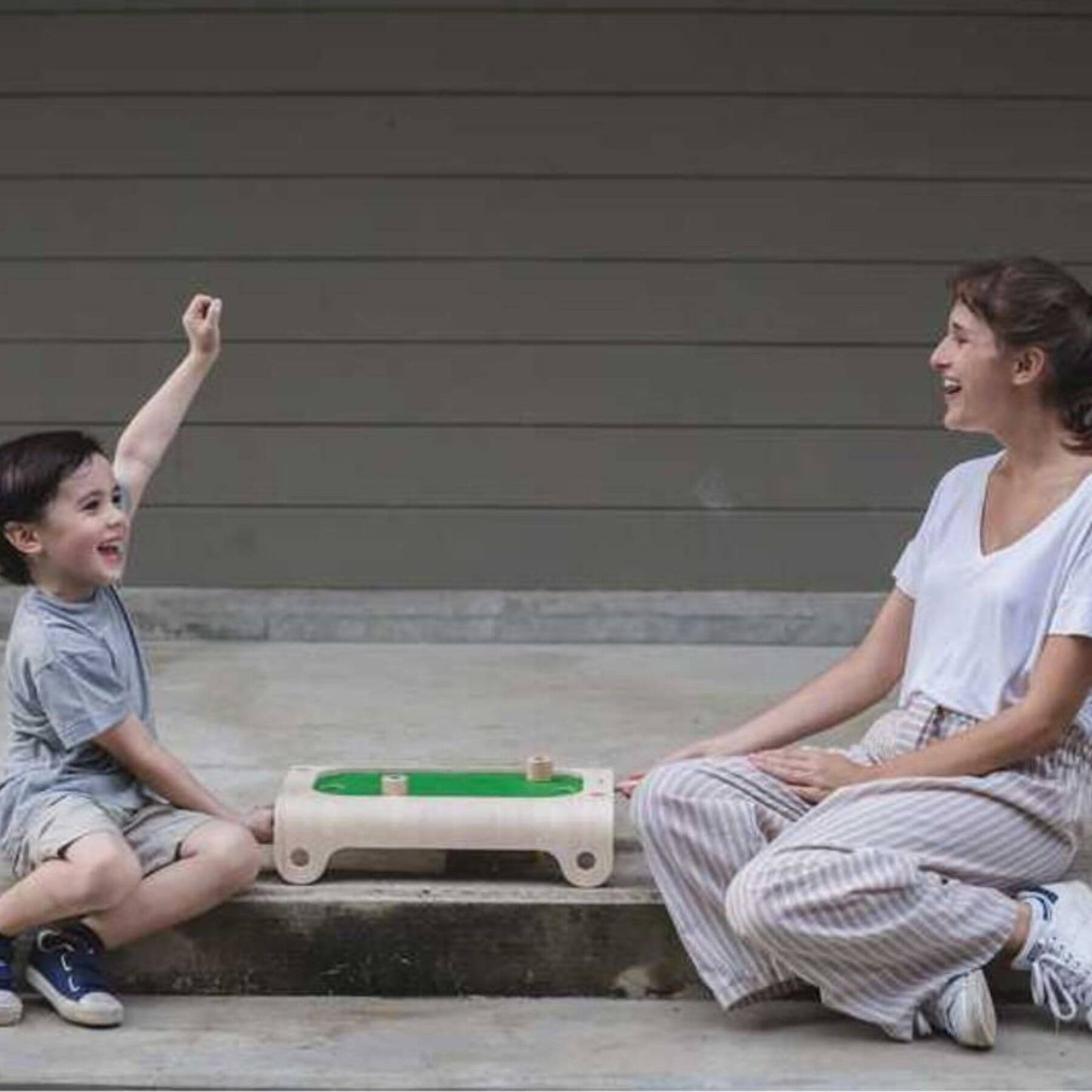 Woman and child playing with PlanToys Magnetic Board Game on a concrete surface.