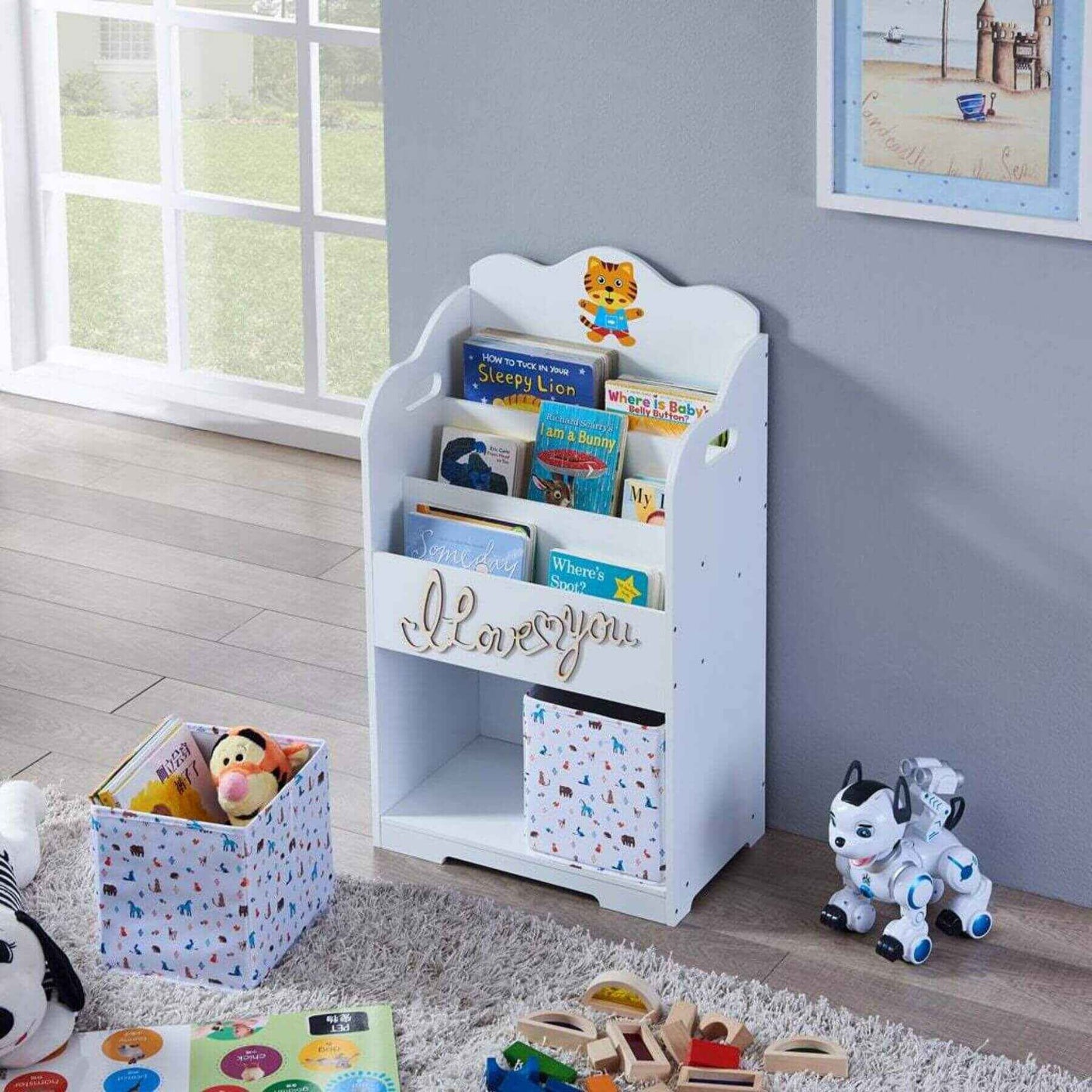 Maison Kids Bookcase with Toy Storage with books and toys in a room with a window and framed picture on the wall.