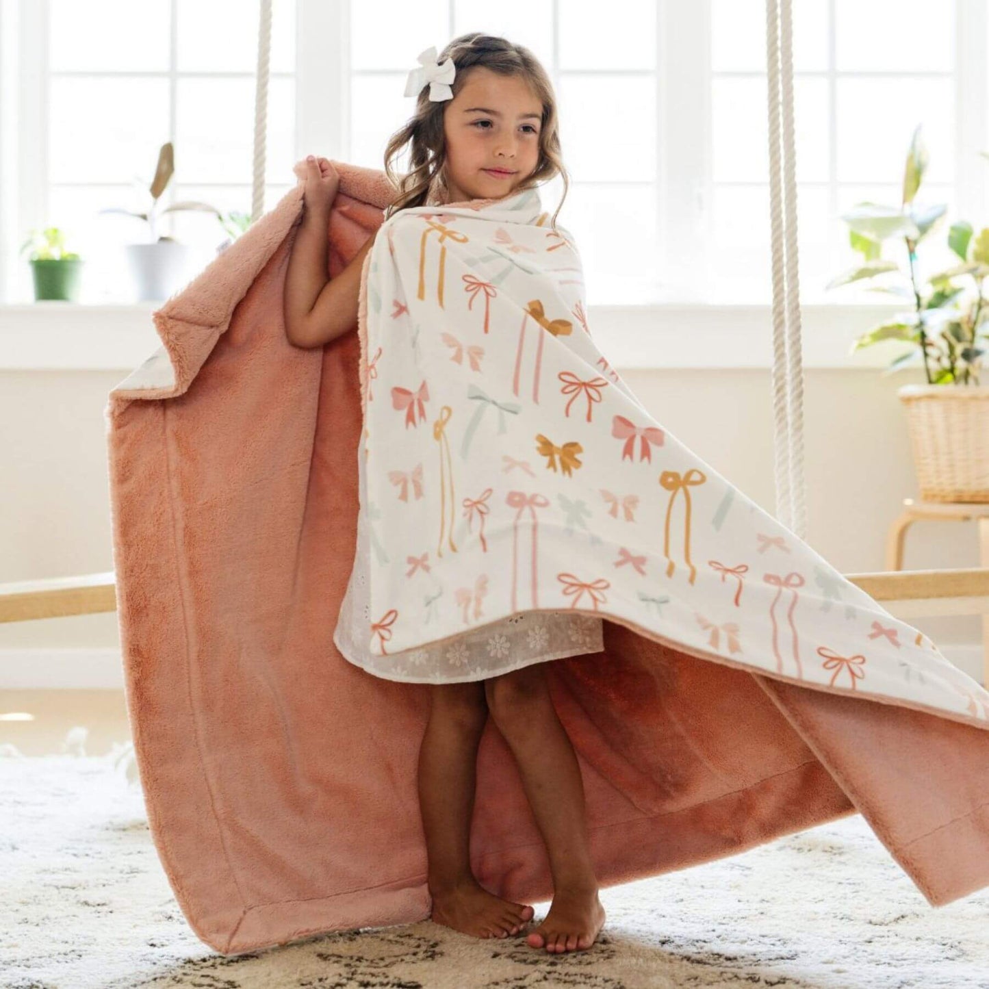 Young girl wrapped in Saranoni Minky/Lush Toddler Blanket with bow pattern indoors