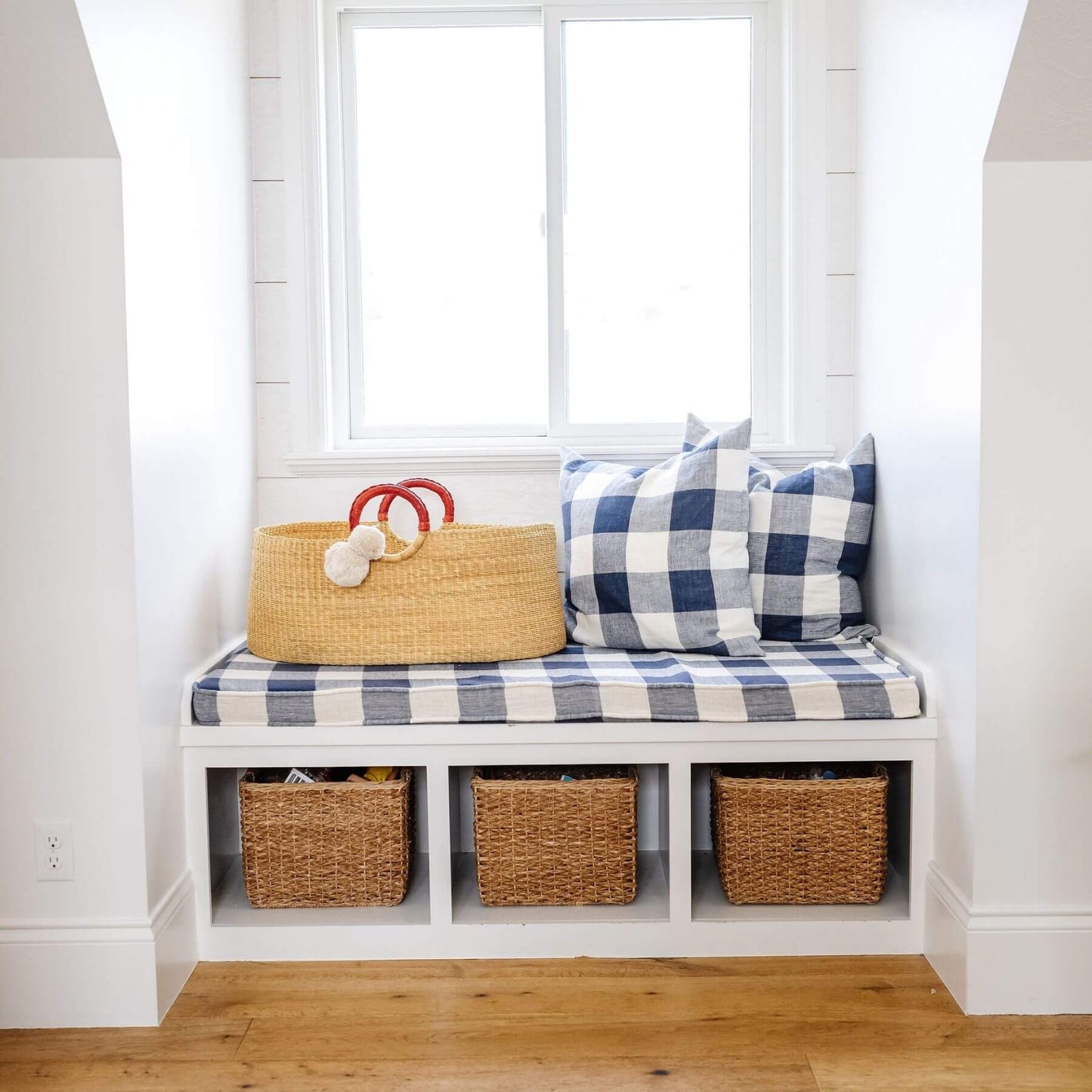 Bench with plaid cushion, African Moses Basket Cognac Circle Handle, and checkered pillows in a bright room.