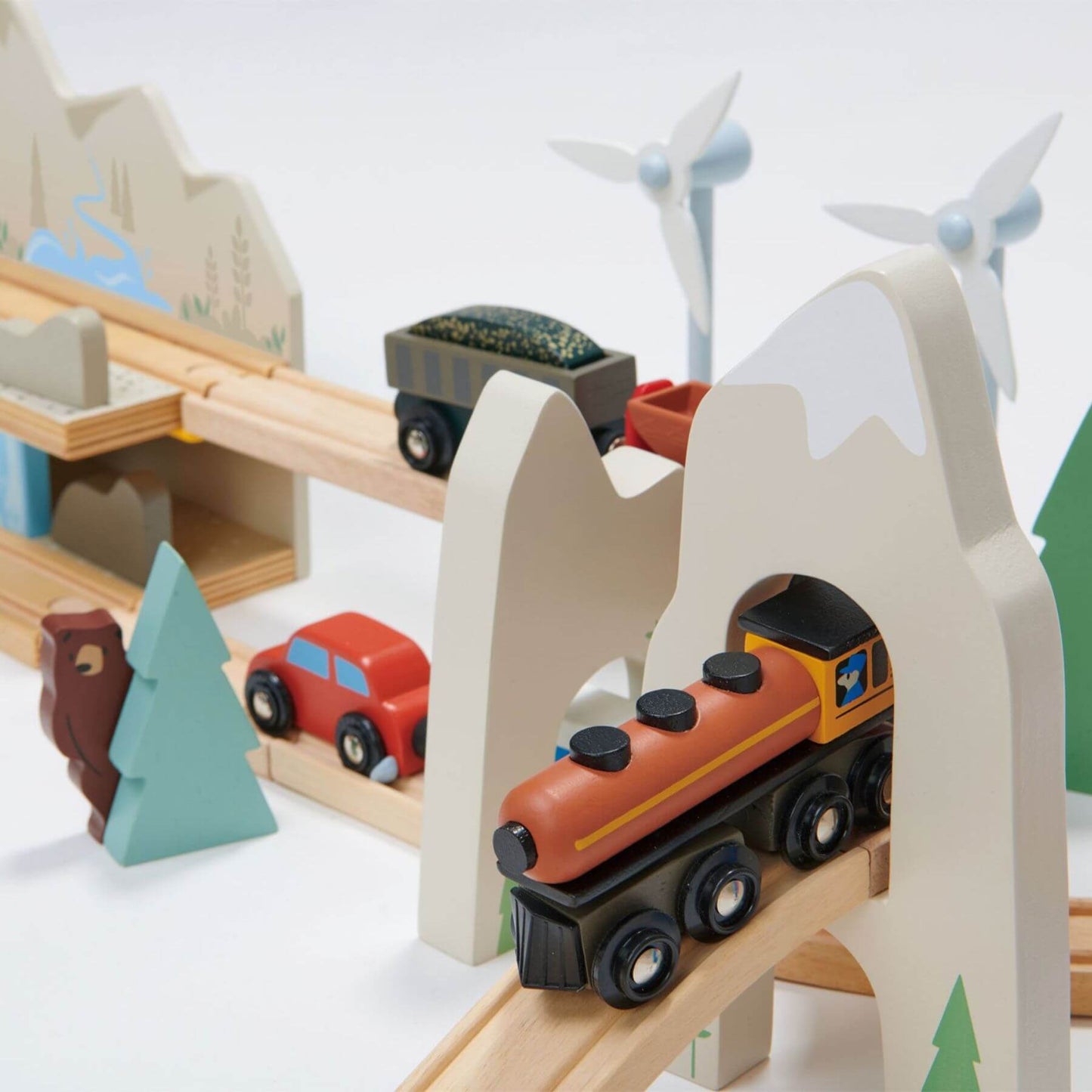 Wooden toy train set with mountains, cars, and wind turbines on a white background