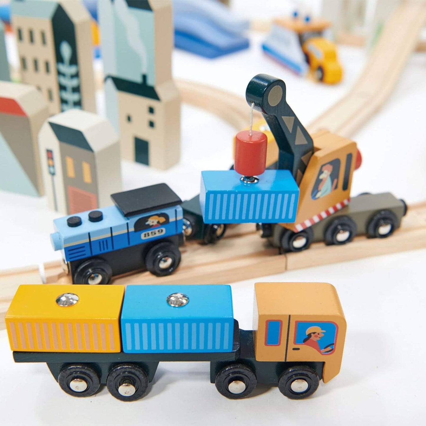 Wooden toy truck and train set on a track with buildings in the background