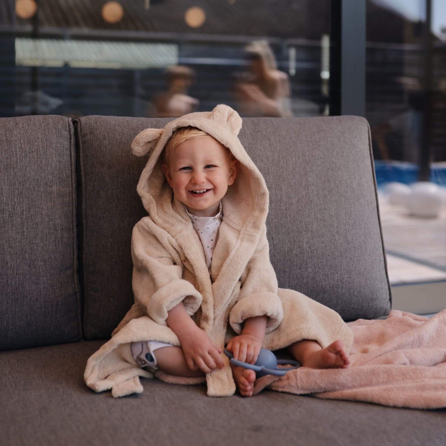 Child in Mushie Bear Robe sitting on a couch indoors.