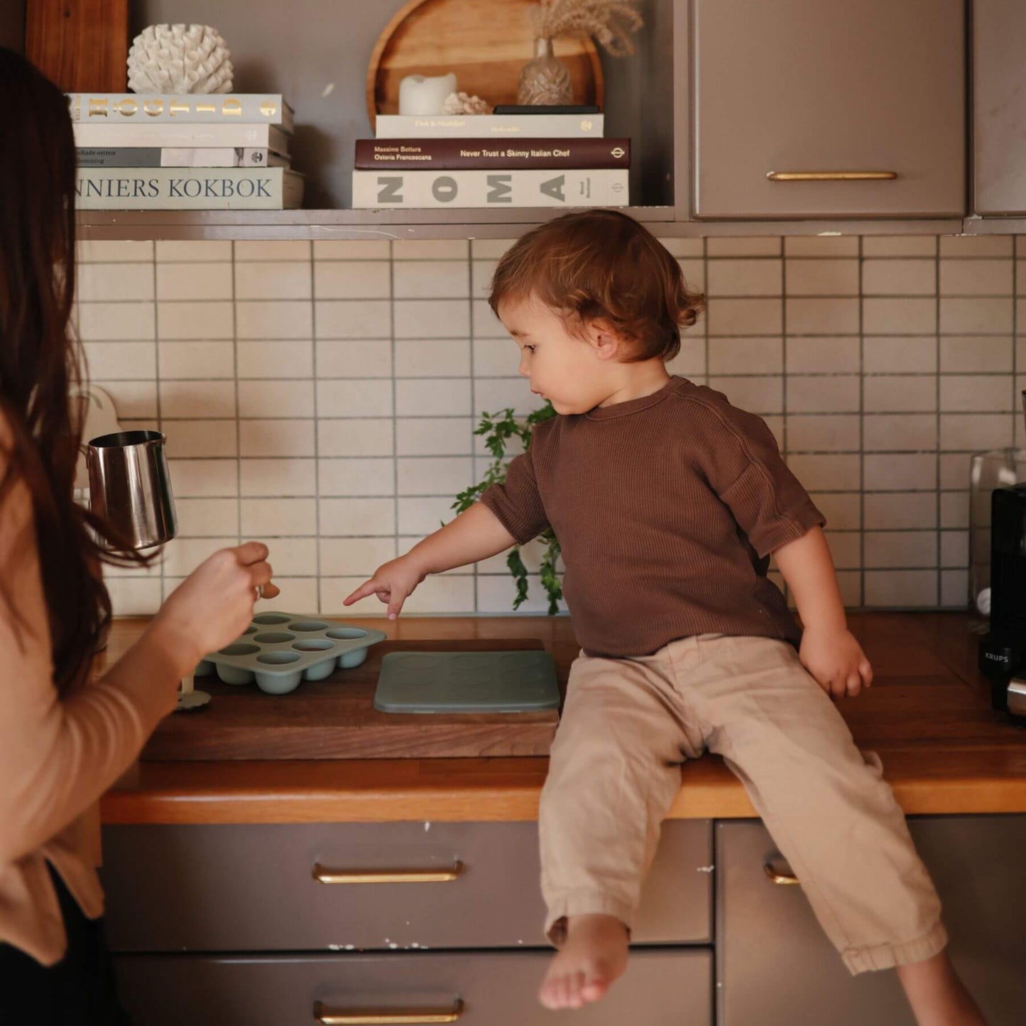 Child sitting on a kitchen counter reaching towards Mushie Baby Food Freezer Tray