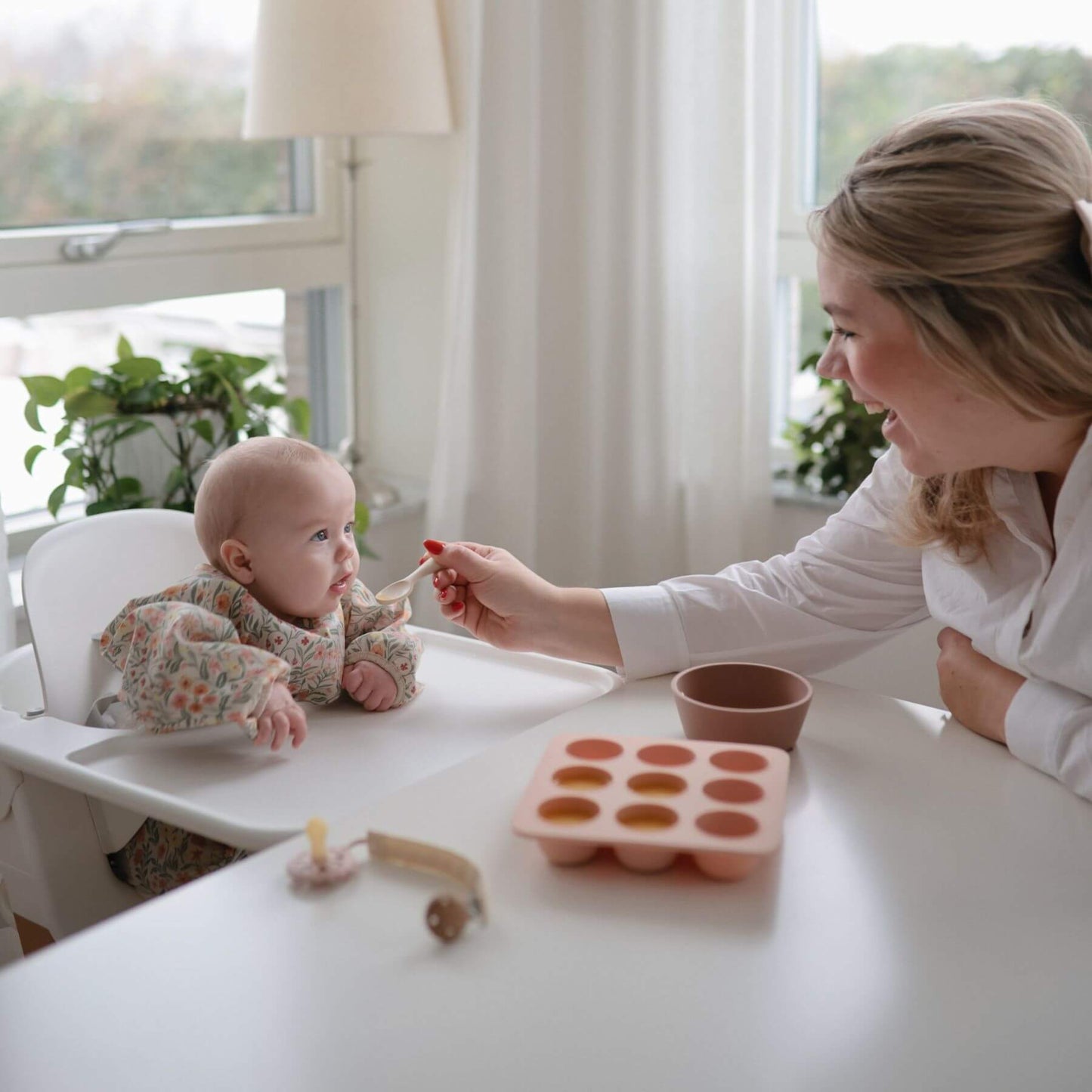 Woman feeding a baby in a high chair with a Mushie Baby Food Freezer Tray on a white table