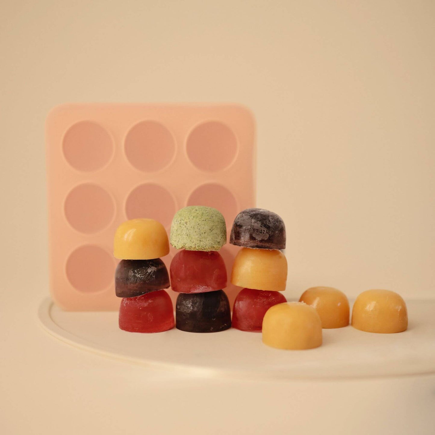 Colorful gummy bears in front of a Mushie Baby Food Freezer Tray on a beige background
