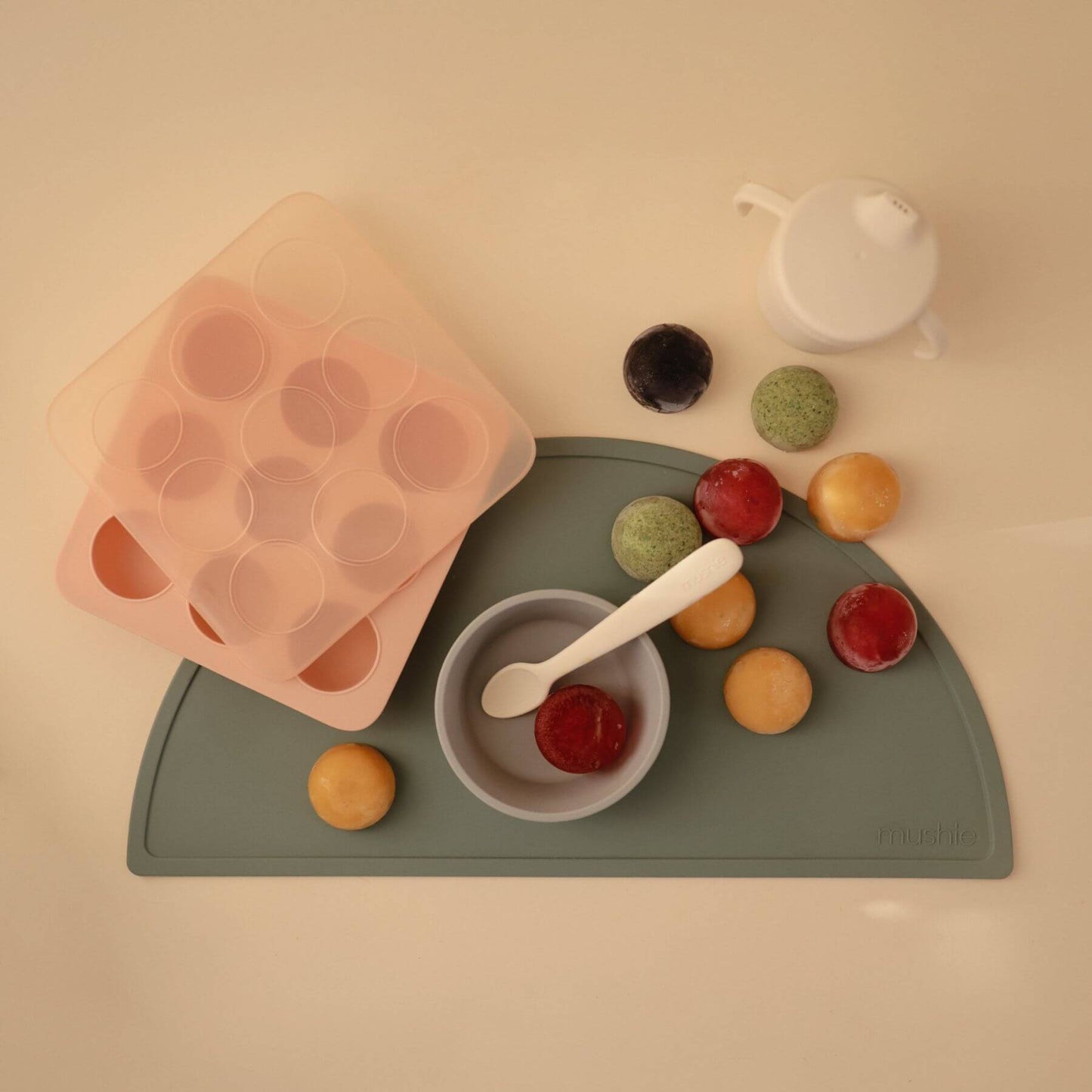 Mushie Baby Food Freezer Tray, green mat with food items and a bowl on a beige background