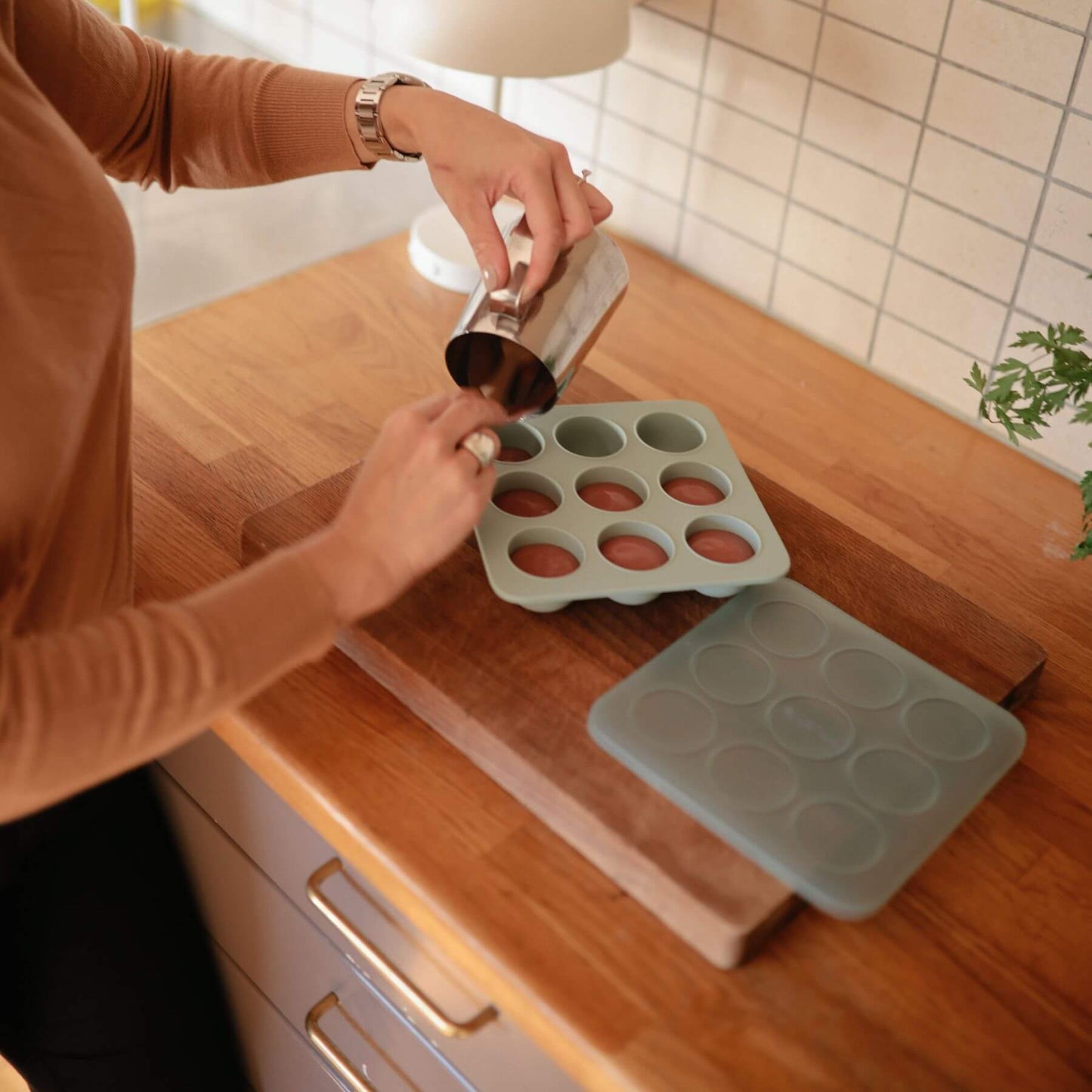 Person using a measuring cup to pour liquid into Mushie Baby Food Freezer Tray Cambridge Blue on a wooden countertop.