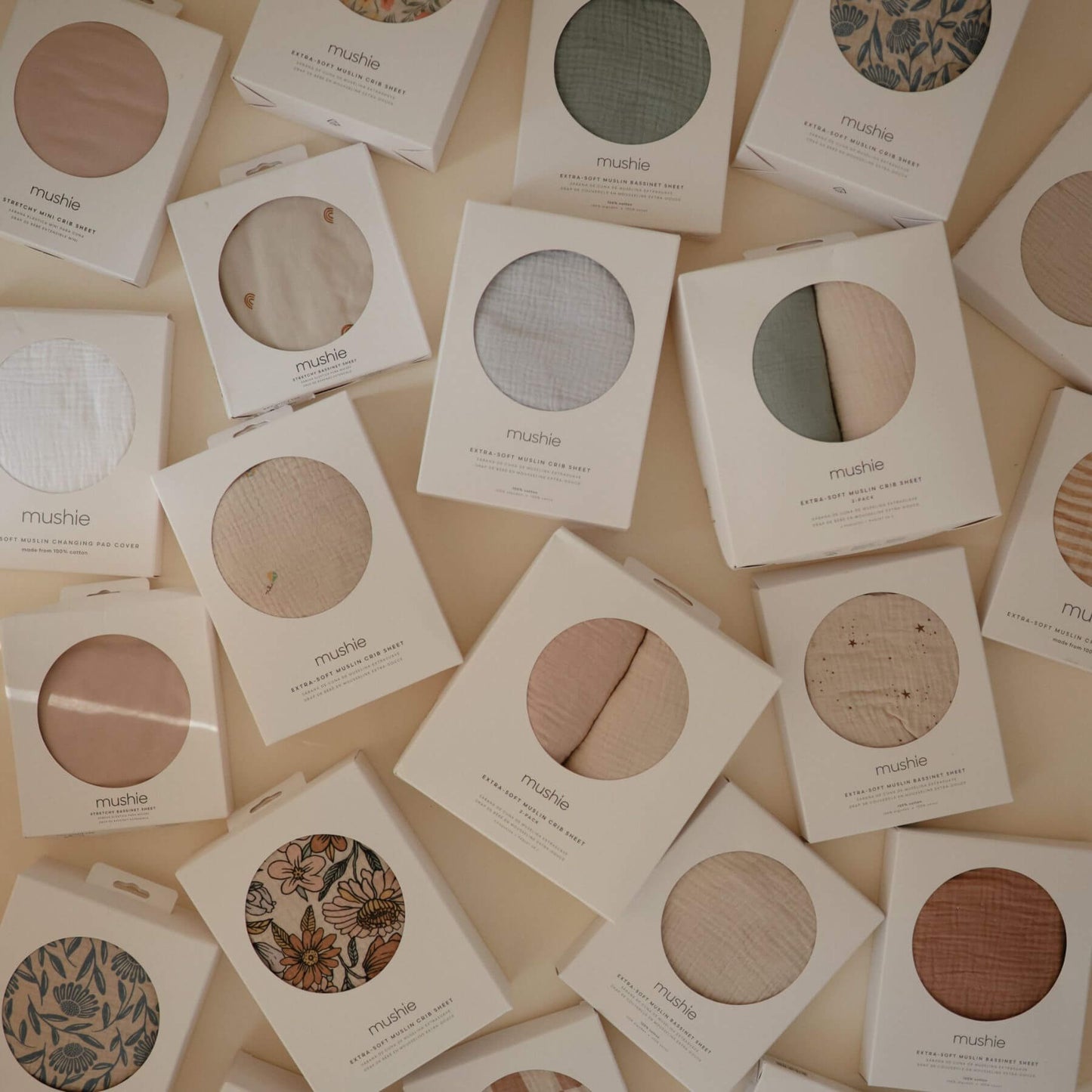 Collection of mushie muslin crib sheets in packaging on a beige background