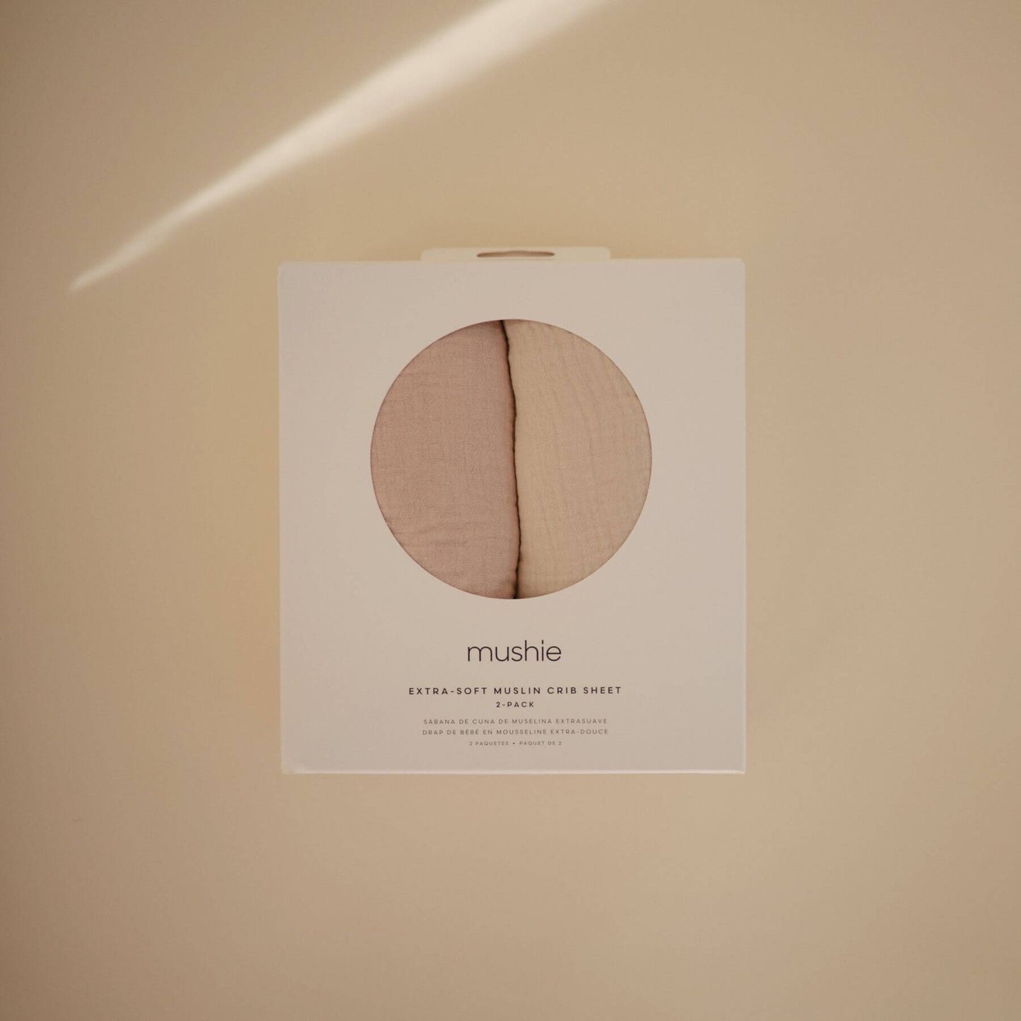 Mushie extra soft muslin crib sheet packaging on a beige background