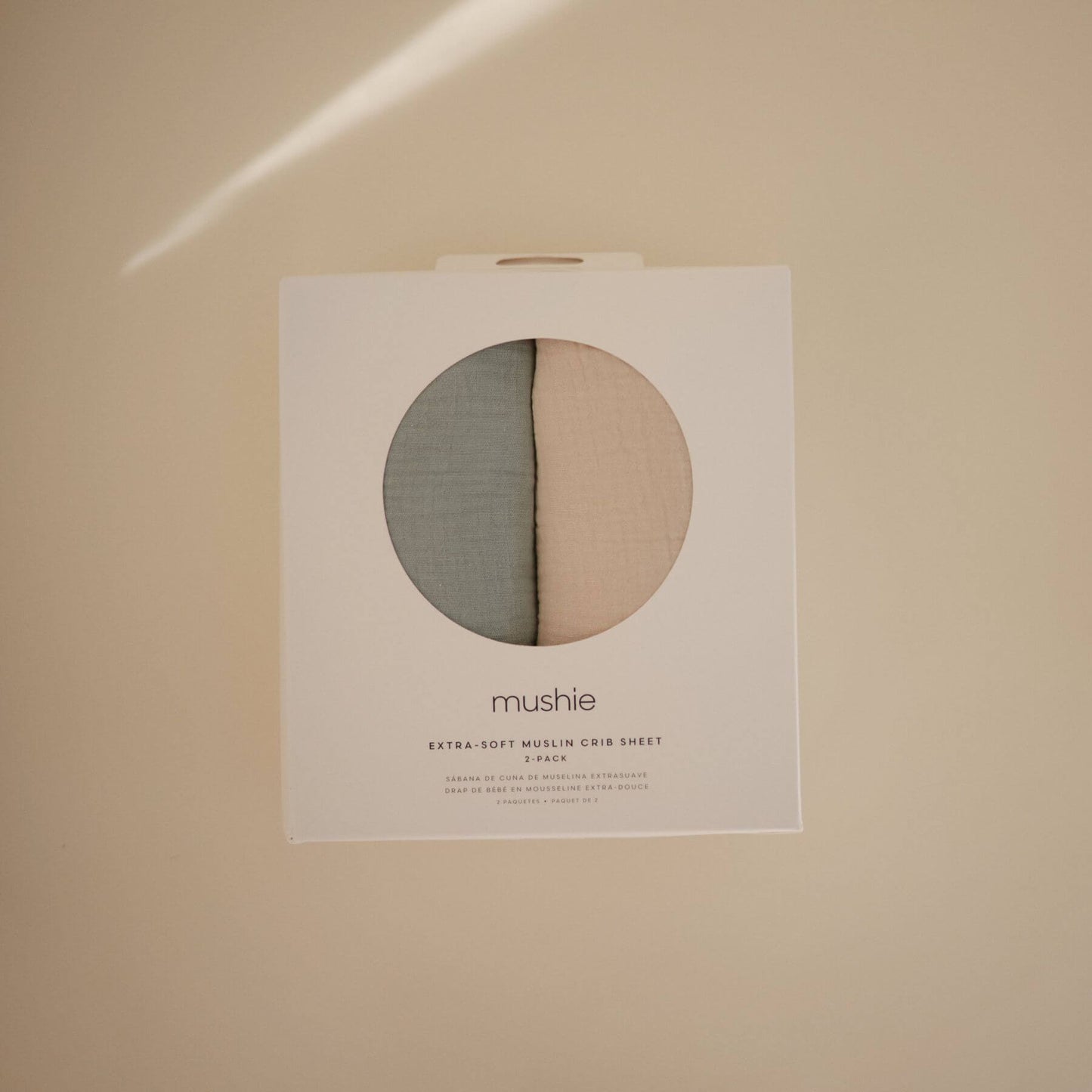 Mushie crib sheet packaging on a beige background