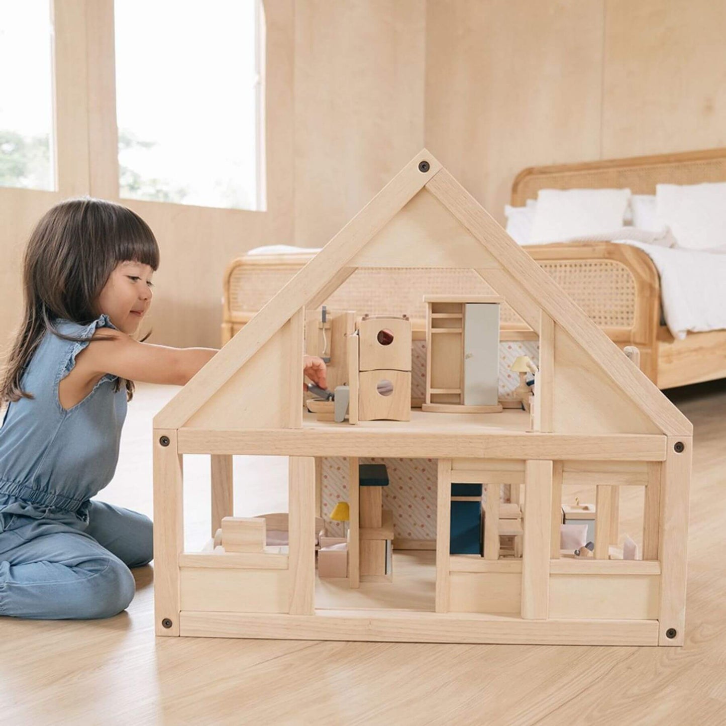 Child playing with PlanToys My First Dollhouse in a room with a bed and window.