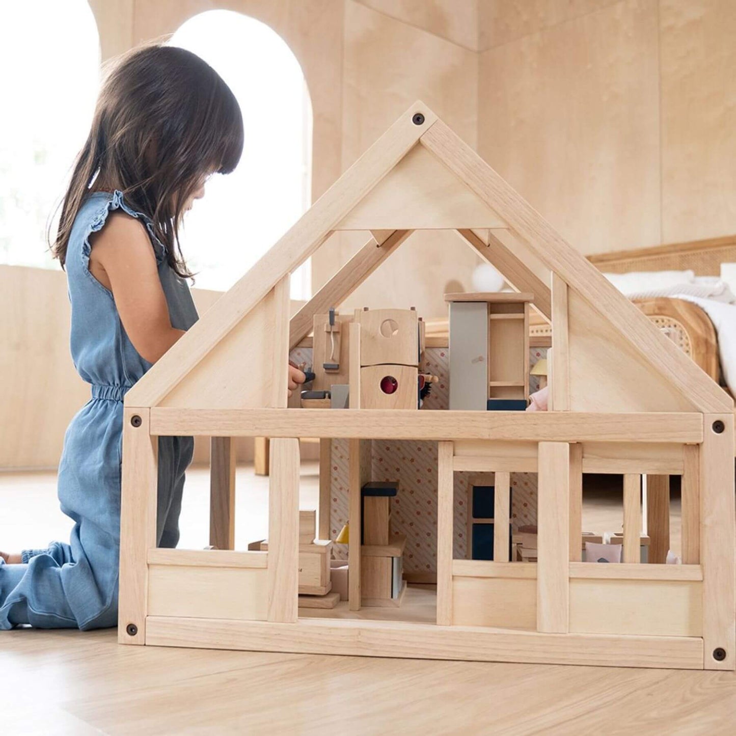 Child playing with PlanToys My First Dollhouse on a light wooden floor.