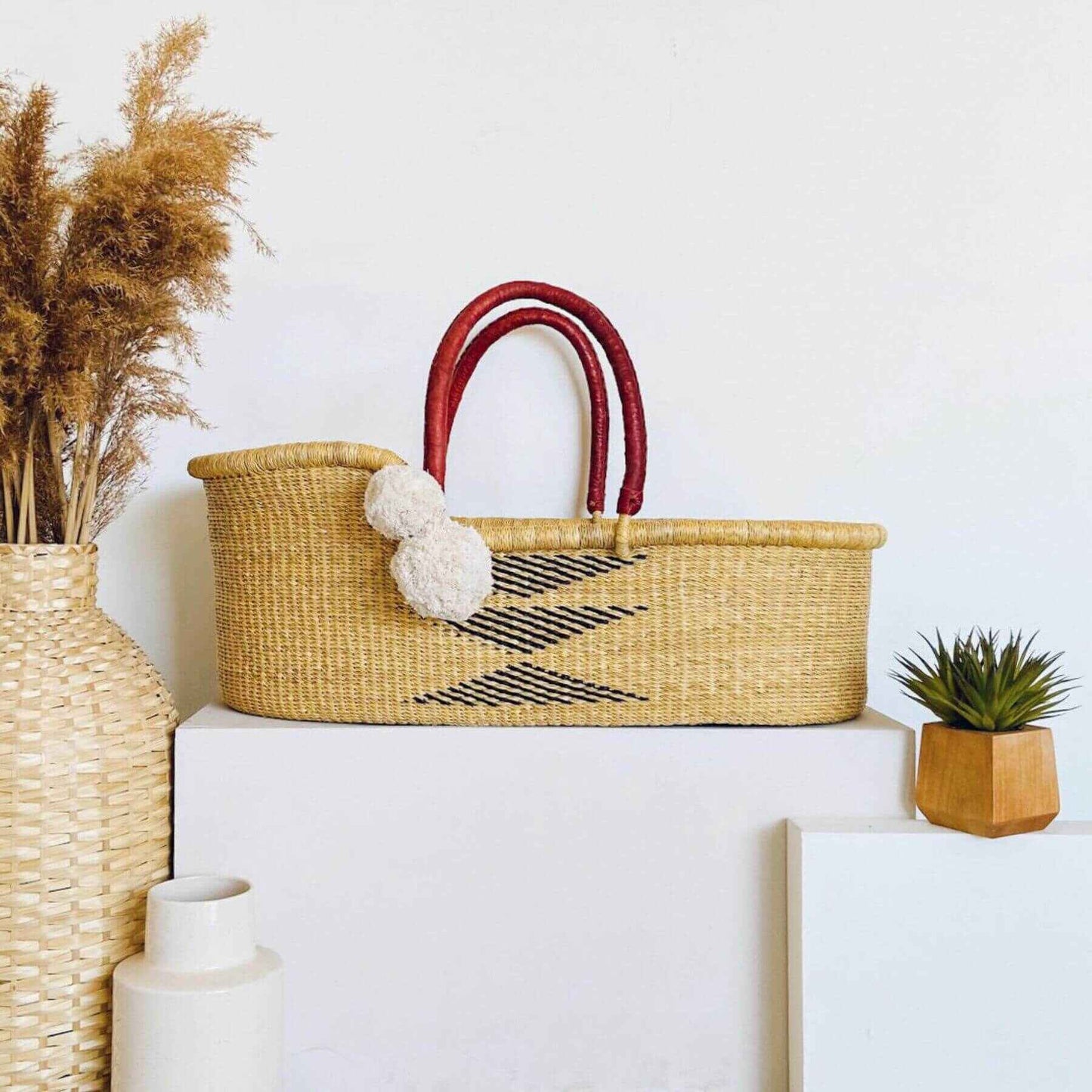 Plum+Sparrow Oak African Moses Basket on a white surface, surrounded by decorative items.