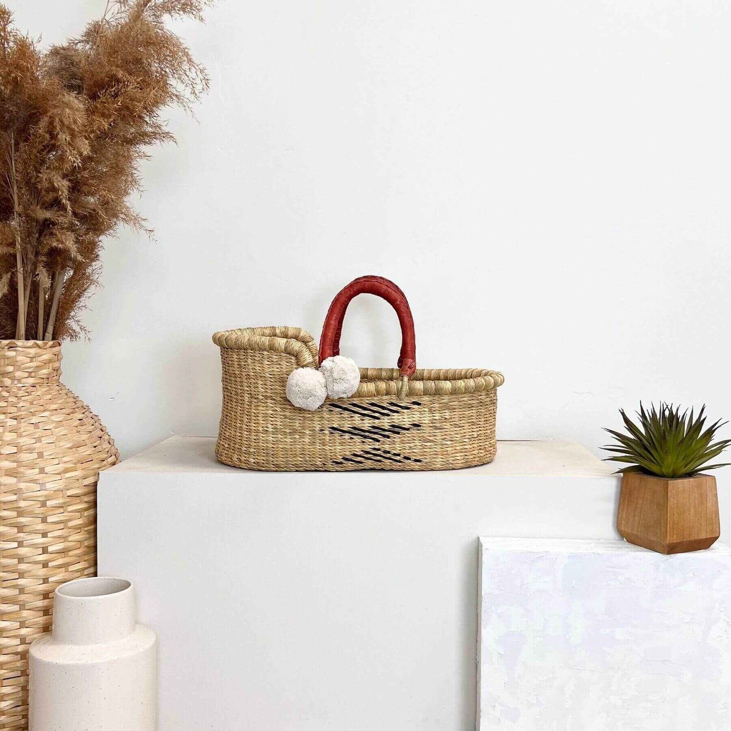 Plum+Sparrow Oak Mini Moses Basket on a white surface with decorative items.