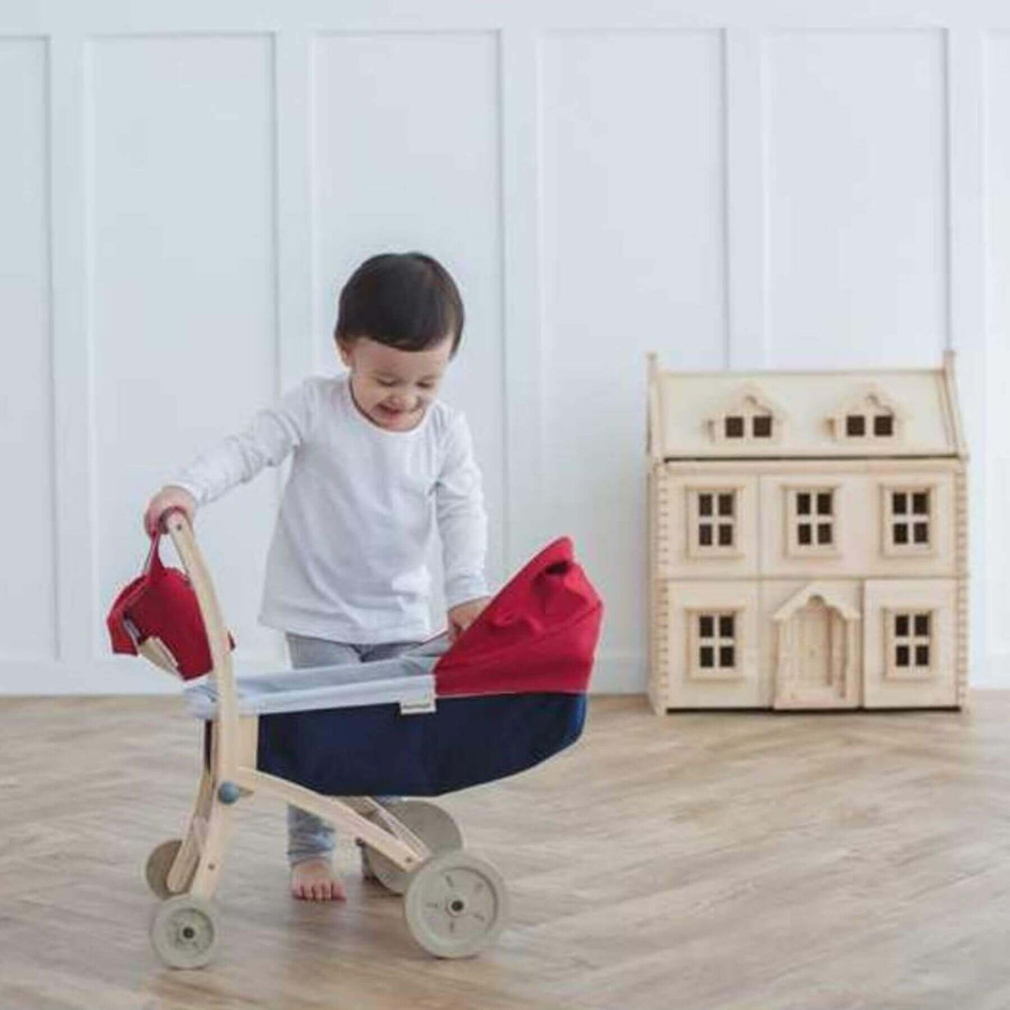 Child playing with PlanToys Doll Stroller and a dollhouse in a room.