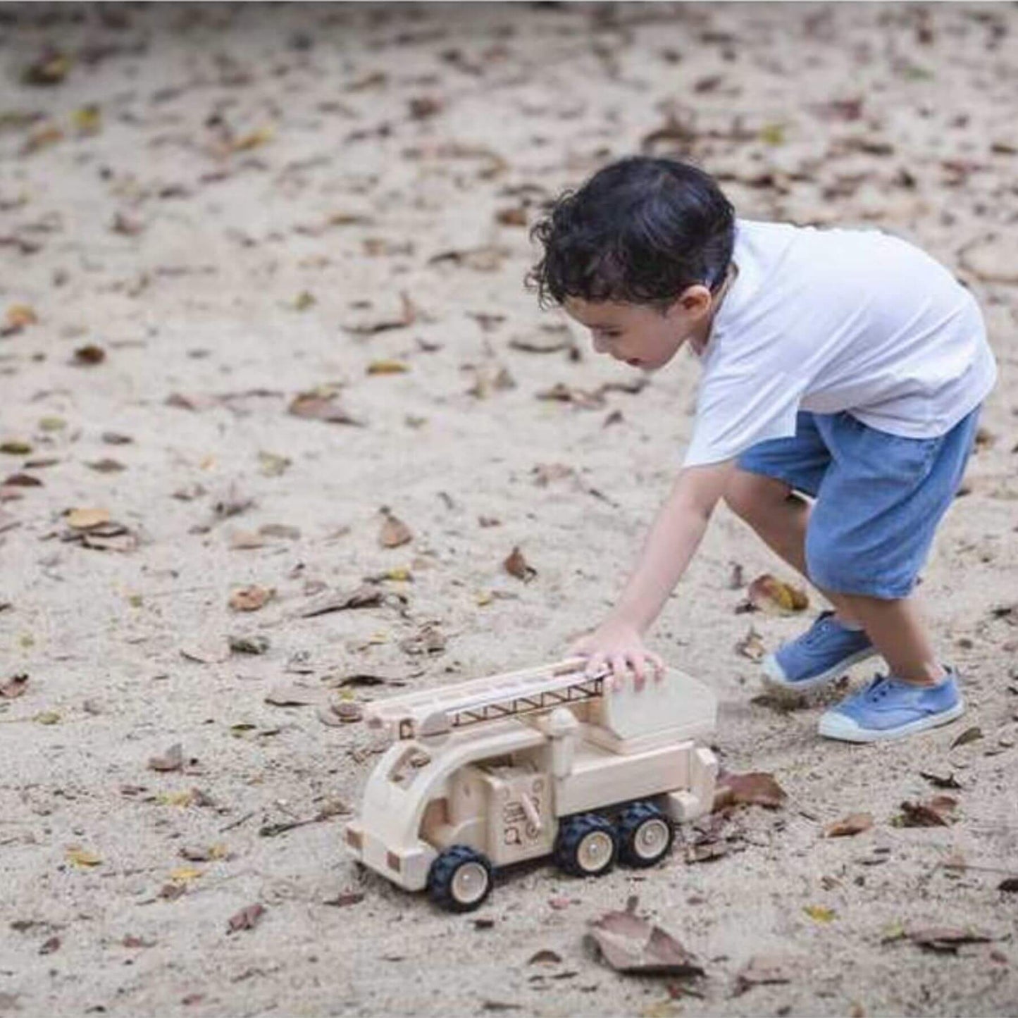 Child playing with PlanToys Fire Truck on sandy ground
