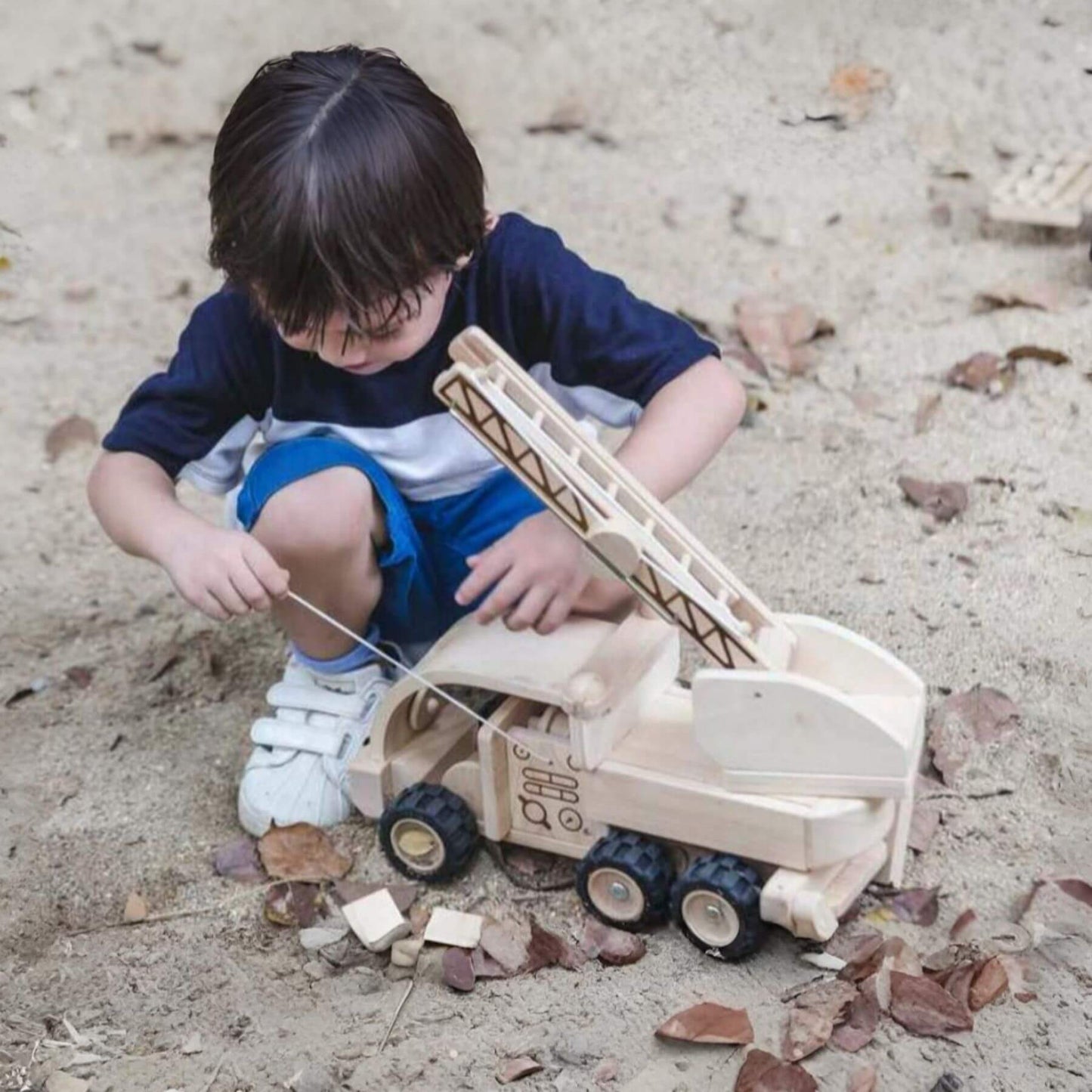 Child playing with PlanToys Fire Truck on sandy ground